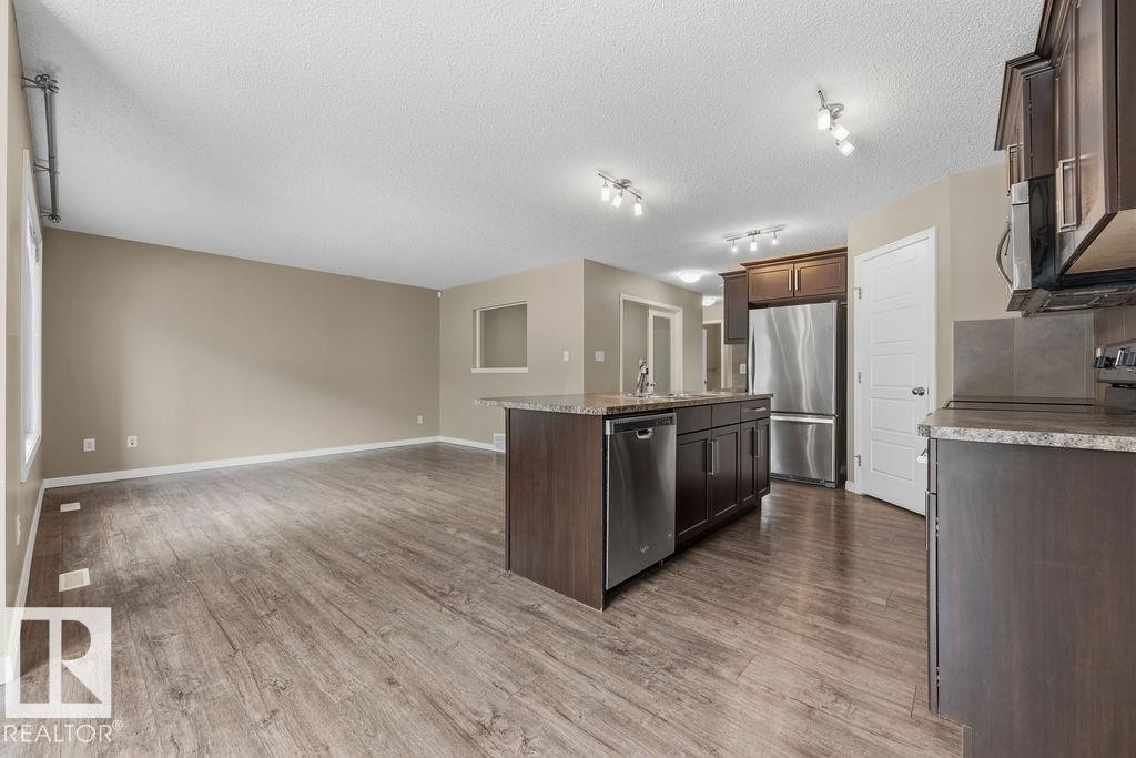 The kitchen features dark wood cabinetry, stainless steel appliances, and a double basin sink - 7873 170A Avenue, Edmonton, AB - Indoor Photo Showing Kitchen With Stainless Steel Kitchen With Double Sink With Upgraded Kitchen