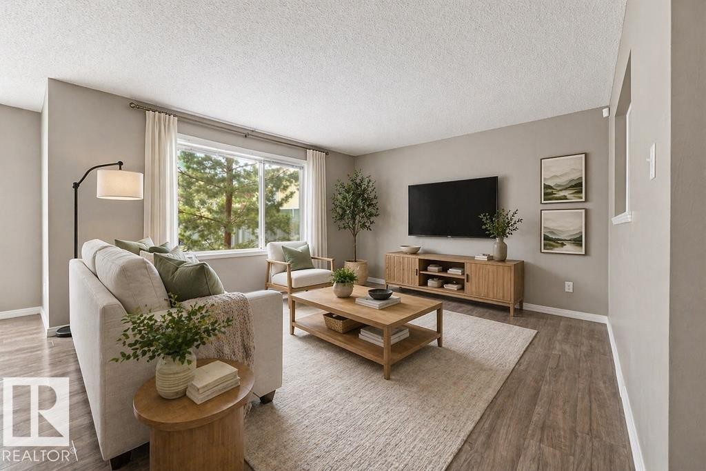 This open concept interior features wood-look flooring, a kitchen island with dark cabinetry, and a large window providing views of the outdoor deck and surrounding properties - 7873 170A Avenue, Edmonton, AB - Indoor