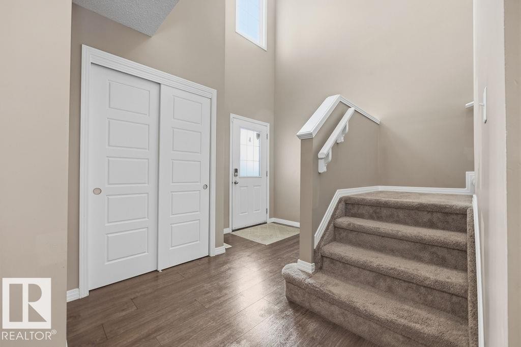 Entryway featuring hardwood style flooring, a carpeted staircase with white railings, and a front door with a decorative glass insert - 7873 170A Avenue, Edmonton, AB - Indoor Photo Showing Other Room