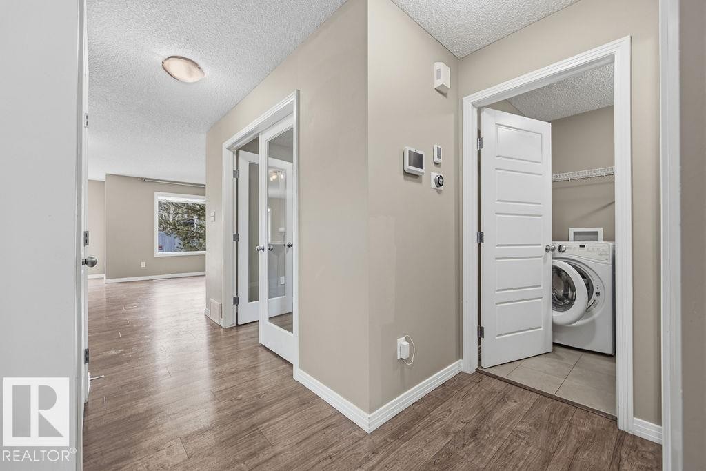 The property features wood-look flooring throughout the main hallway, leading to a room with a window providing natural light - 7873 170A Avenue, Edmonton, AB - Indoor Photo Showing Laundry Room