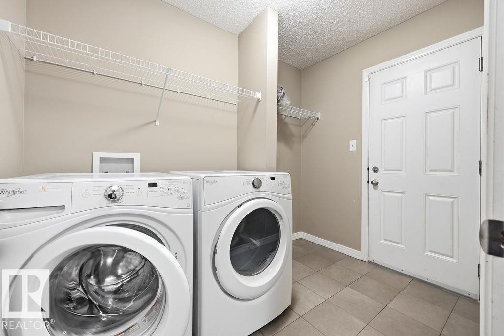 This utility space features a tiled floor, overhead wire shelving, and a paneled door - 7873 170A Avenue, Edmonton, AB - Indoor Photo Showing Laundry Room