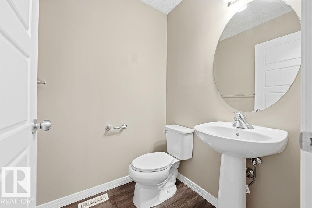 This powder room features a pedestal sink with a chrome faucet, a white toilet, and an oval mirror - 7873 170A Avenue, Edmonton, AB - Indoor Photo Showing Bathroom