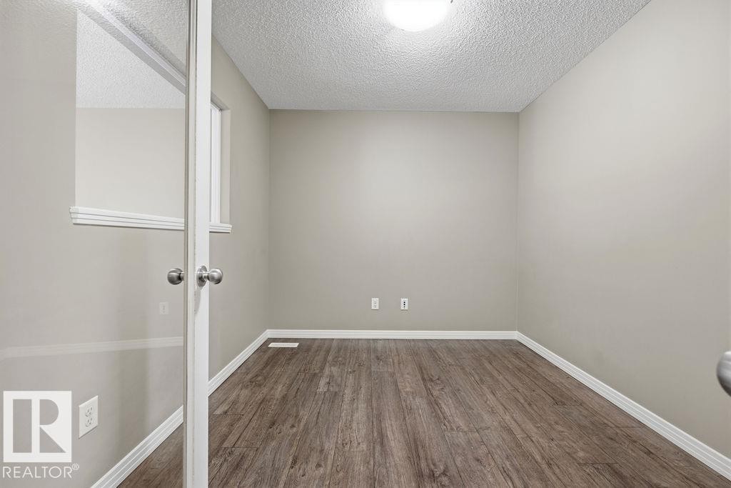 The property features warm-toned hardwood floors, light neutral walls, and white trim - 7873 170A Avenue, Edmonton, AB - Indoor Photo Showing Other Room