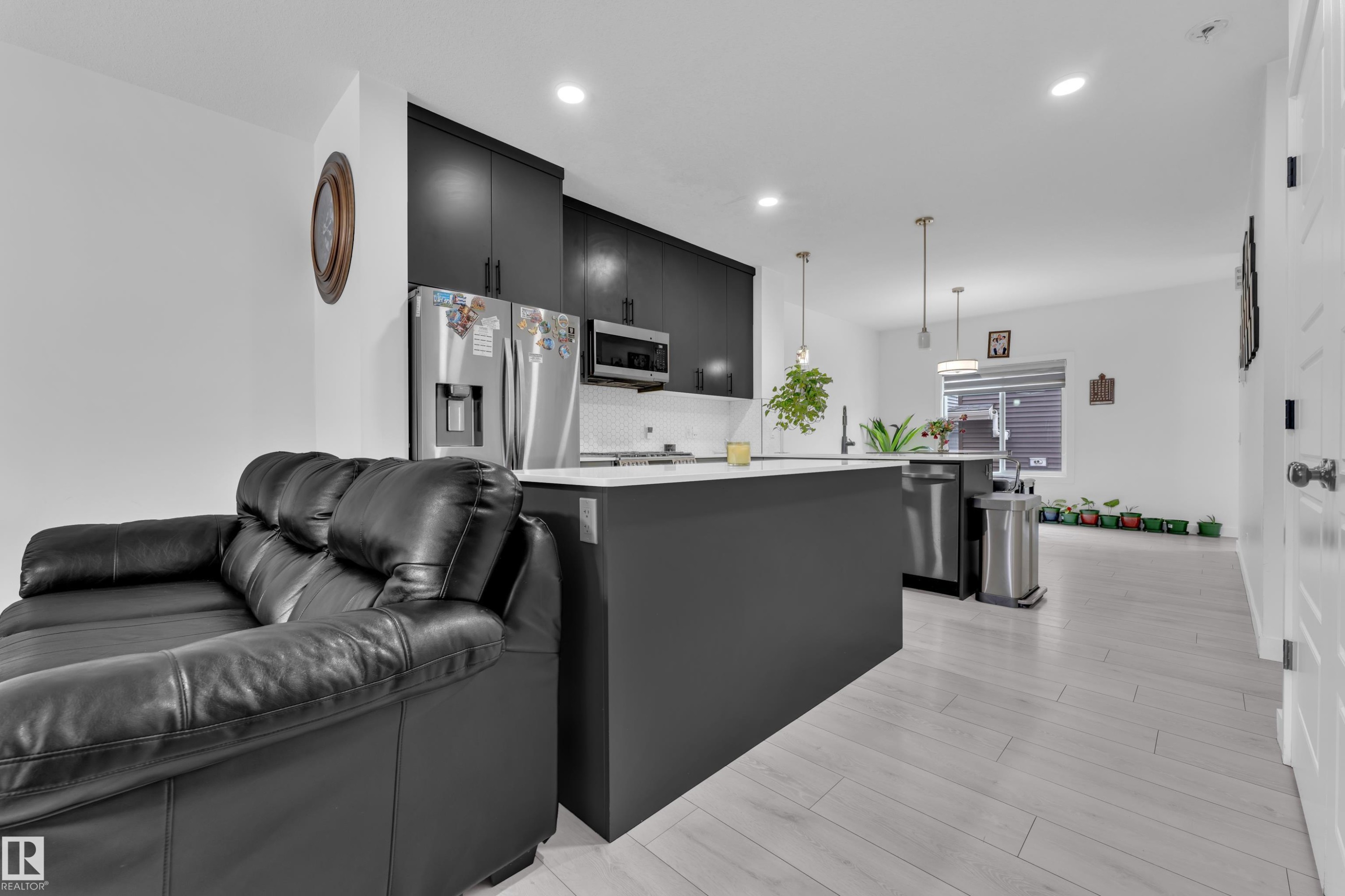 The open-concept living space features light-colored flooring, a kitchen with dark cabinetry, stainless steel appliances, and a central island with a light countertop - 1645 Plum Circle, Edmonton, AB - Indoor Photo Showing Kitchen With Upgraded Kitchen