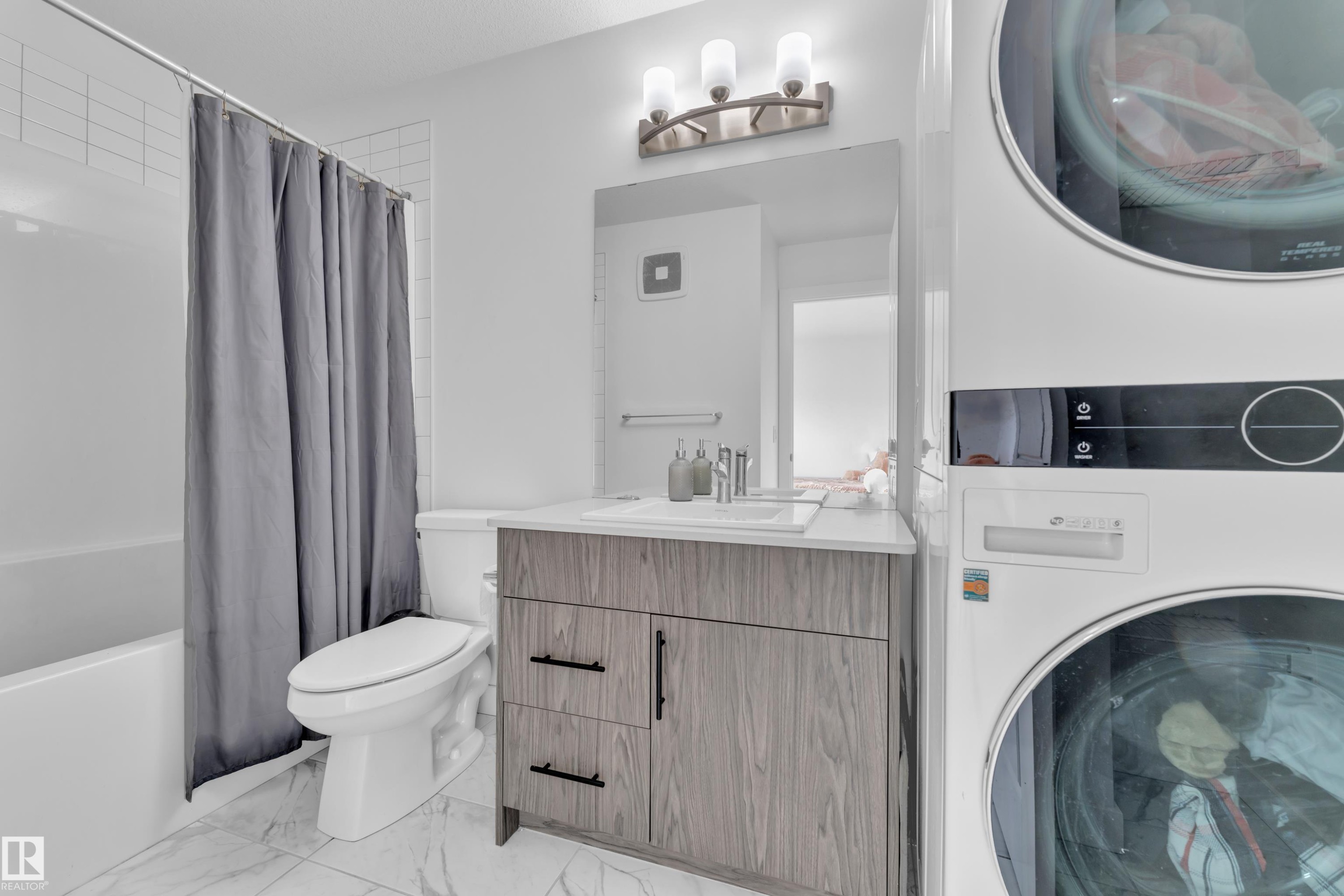 This bathroom features white tiled walls, a toilet, and a vanity with a rectangular sink, a white countertop, and dark-toned cabinetry - 1645 Plum Circle, Edmonton, AB - Indoor Photo Showing Laundry Room