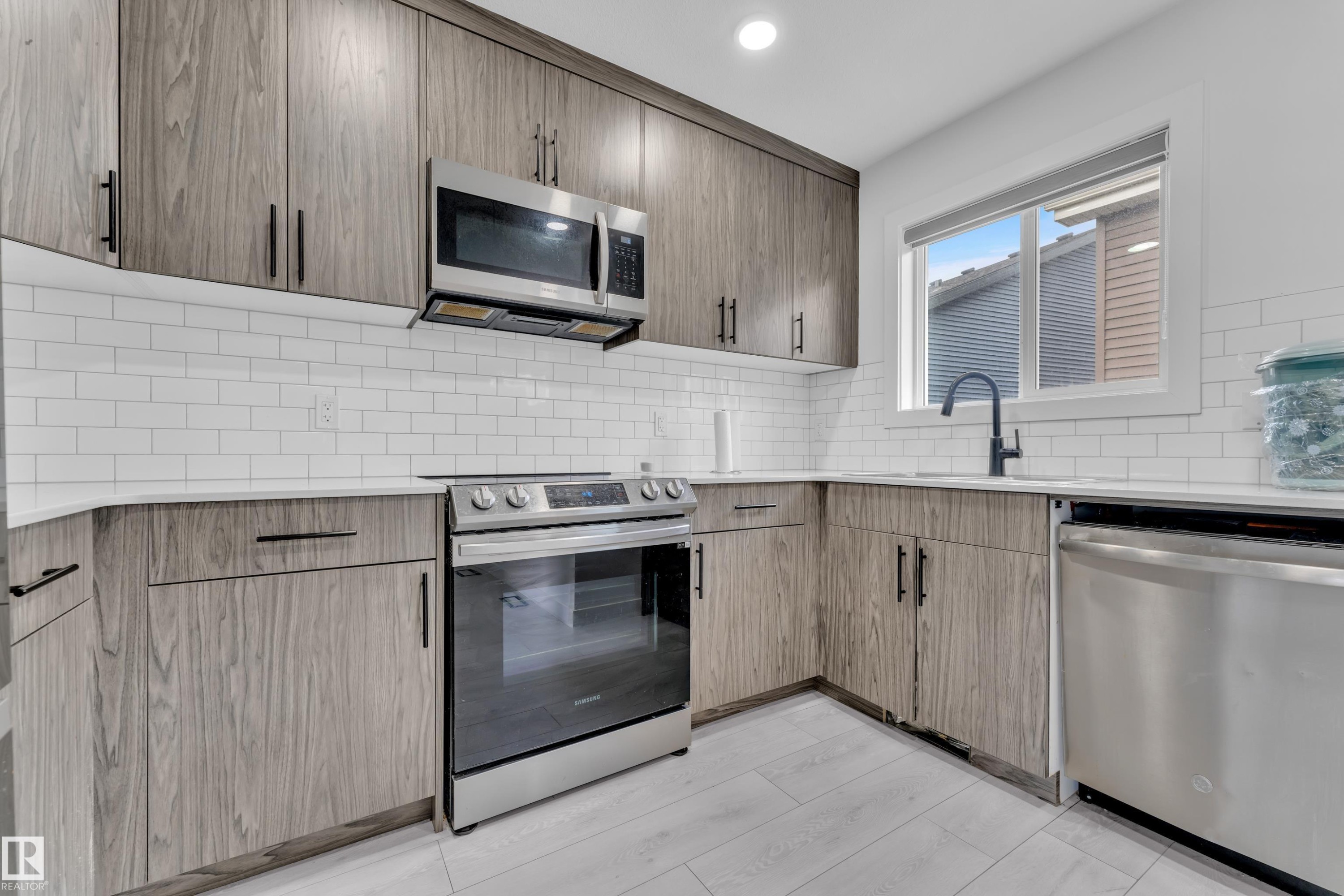 The kitchen features wood-look cabinetry, white subway tile backsplash, and a stainless steel appliance package, including a microwave, range, and dishwasher - 1645 Plum Circle, Edmonton, AB - Indoor Photo Showing Kitchen With Upgraded Kitchen