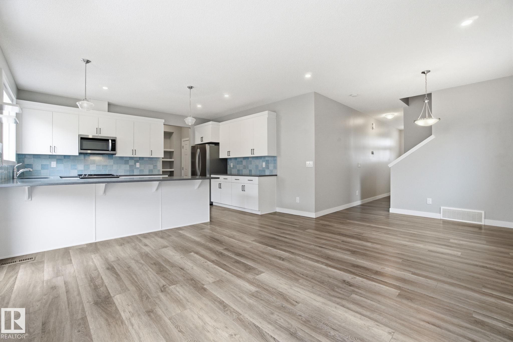 The kitchen features white cabinetry, stainless steel appliances, a light blue tiled backsplash, and recessed lighting - 1607 202 Street, Edmonton, AB - Indoor Photo Showing Kitchen With Upgraded Kitchen