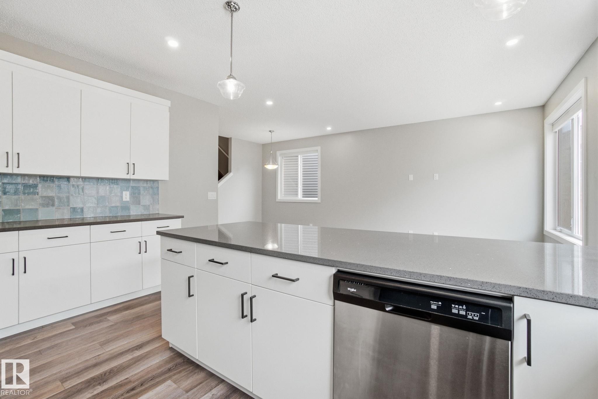 The kitchen features white cabinetry, a light blue tiled backsplash, a gray countertop, and a stainless steel dishwasher - 1607 202 Street, Edmonton, AB - Indoor Photo Showing Kitchen