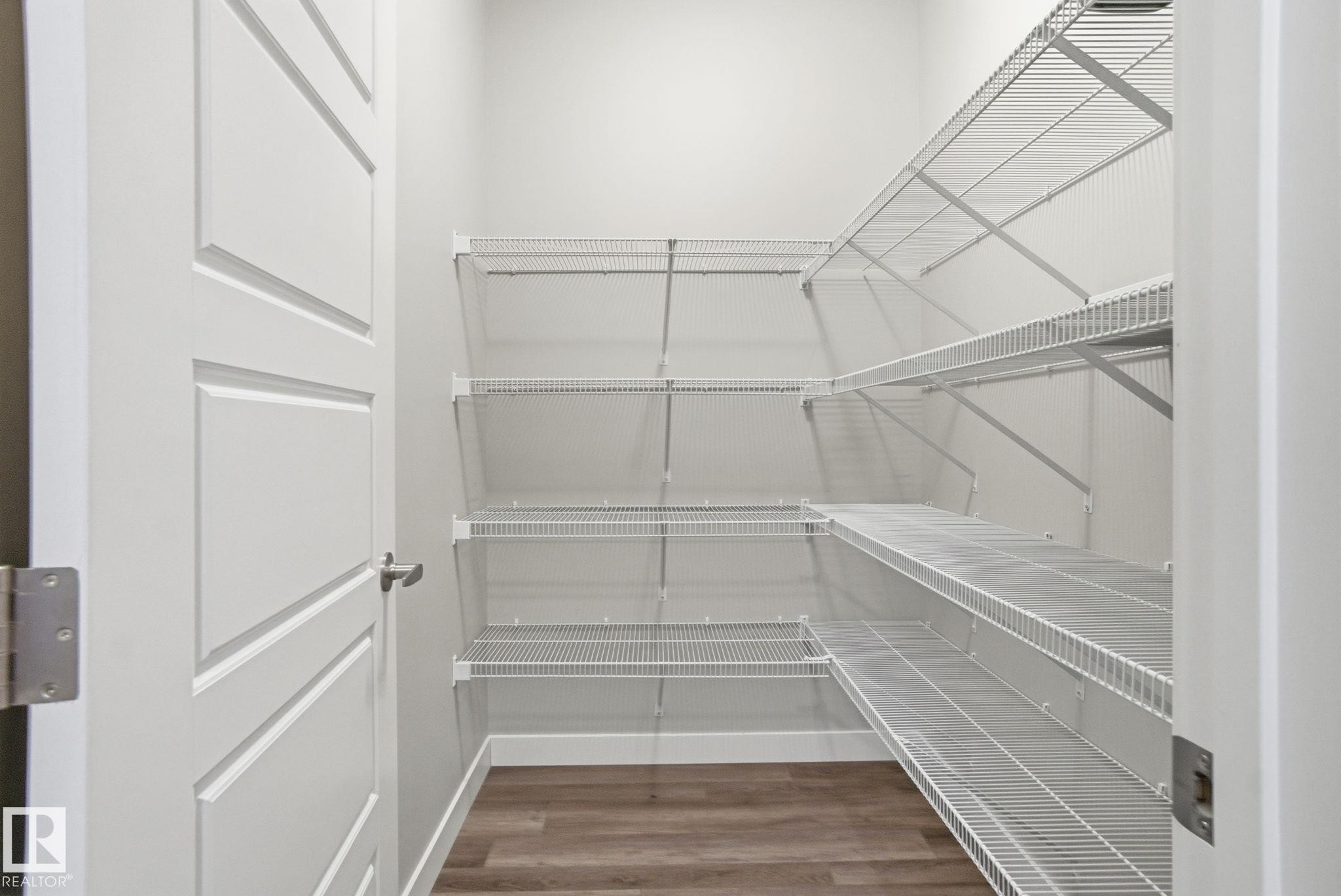 The property features a spacious walk-in closet with extensive wire shelving, a wood-look floor, and white walls - 1607 202 Street, Edmonton, AB - Indoor With Storage