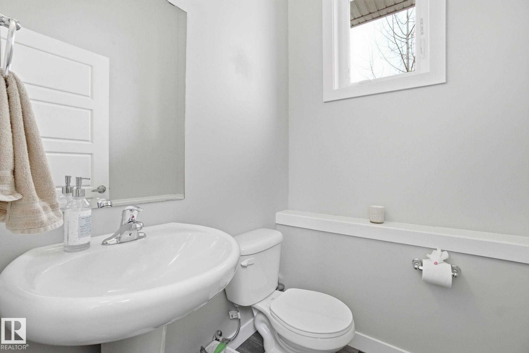 This bathroom features a pedestal sink with a chrome faucet, a wall-mounted mirror, and a toilet - 1607 202 Street, Edmonton, AB - Indoor Photo Showing Bathroom
