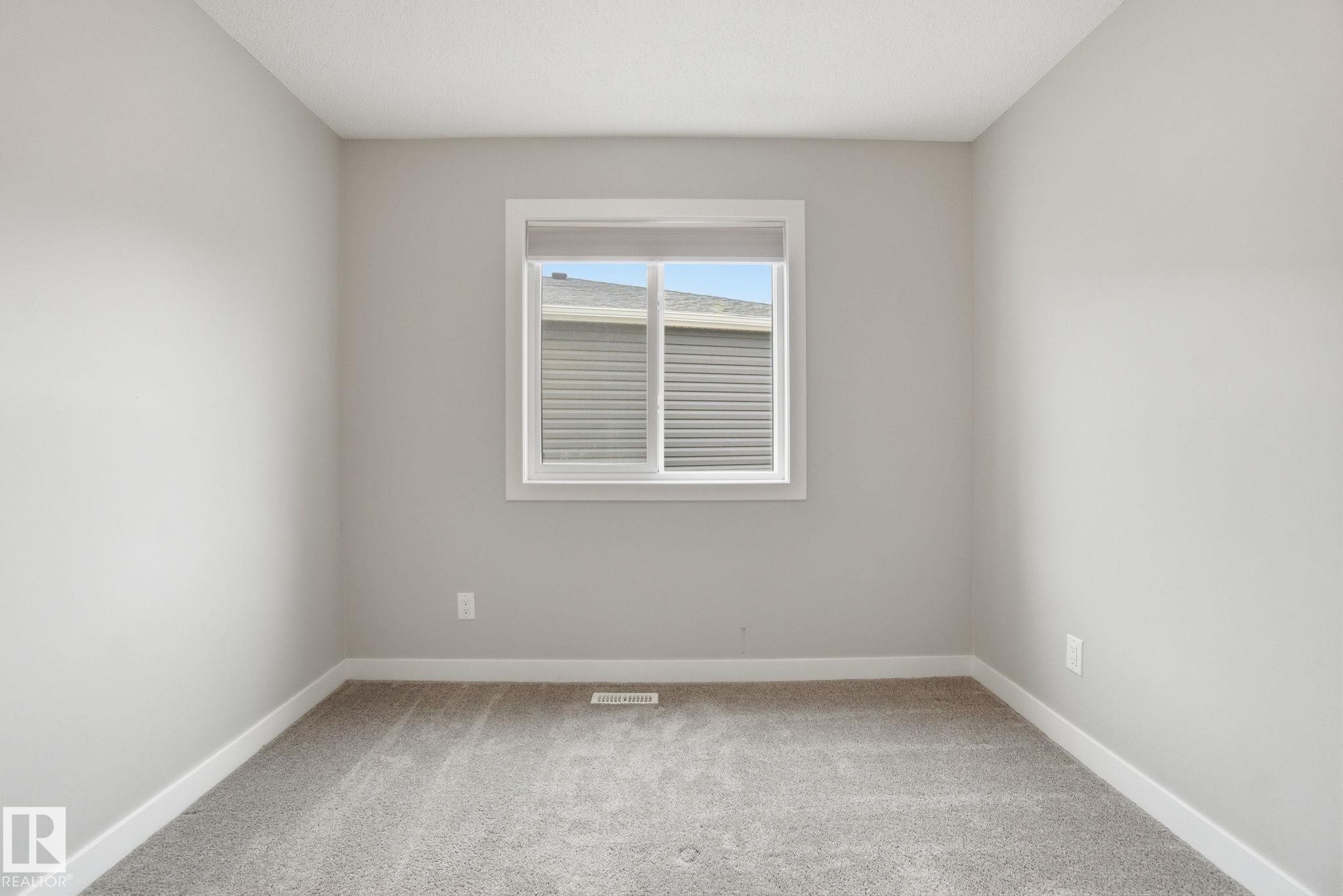 This room features light grey walls, a white framed window, and grey carpet flooring - 1607 202 Street, Edmonton, AB - Indoor Photo Showing Other Room
