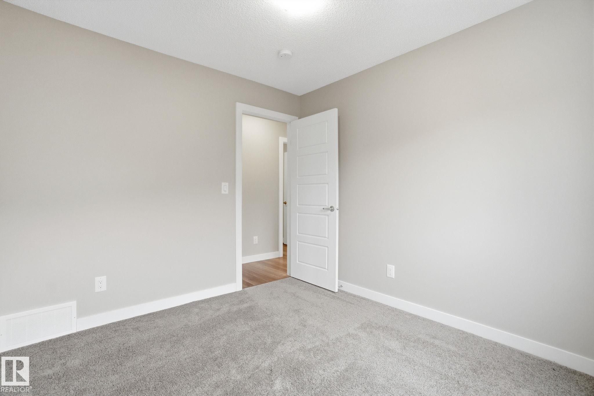 This room features light grey carpeting, light grey walls, white trim, and a white interior door - 1607 202 Street, Edmonton, AB - Indoor Photo Showing Other Room