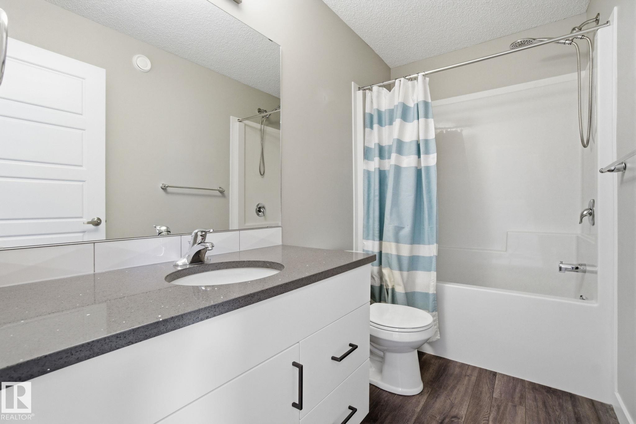 Bathroom featuring a vanity with a light gray countertop and a white cabinet, a built-in sink with a chrome faucet, and a shower-tub combination with a chrome shower head and fixtures - 1607 202 Street, Edmonton, AB - Indoor Photo Showing Bathroom