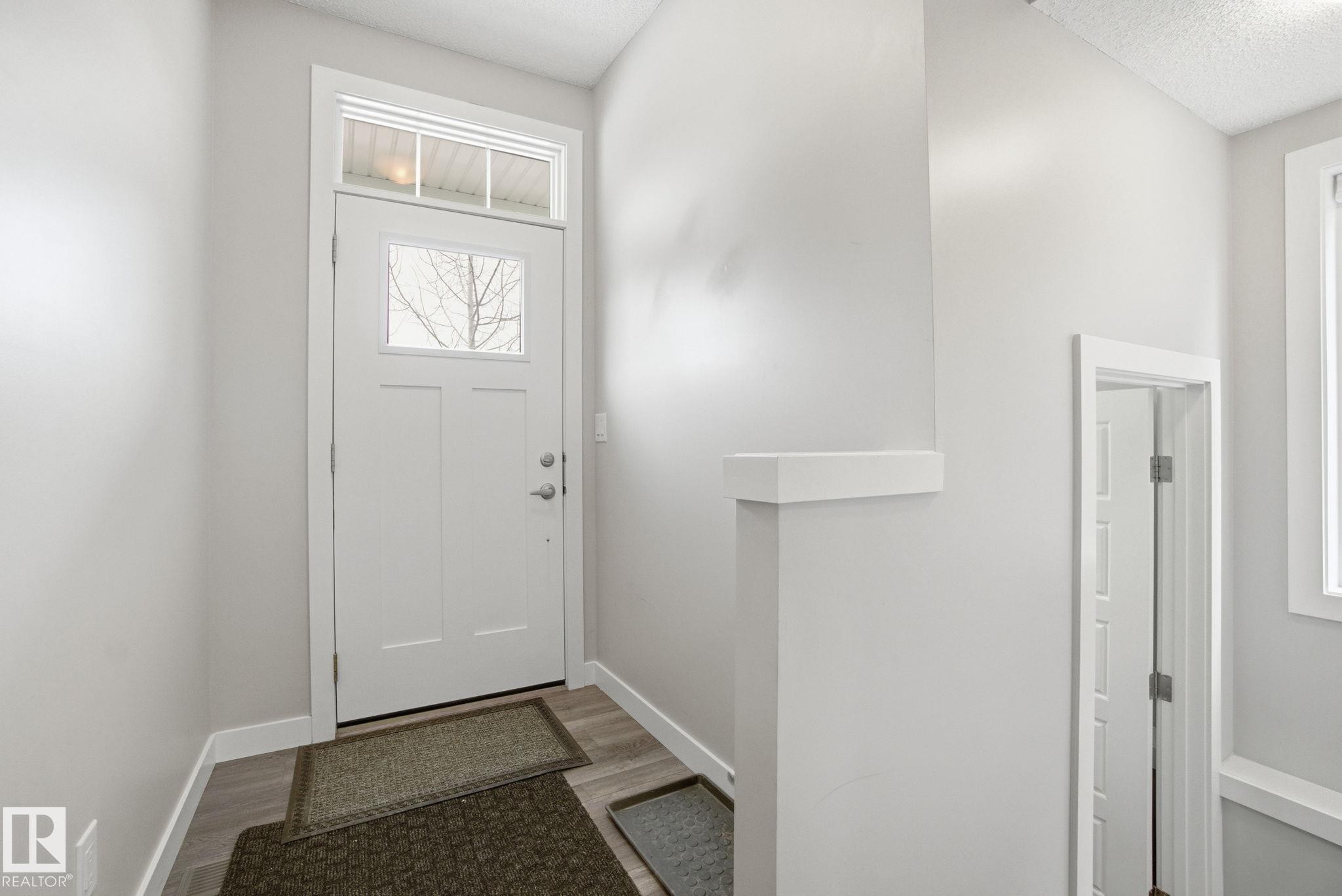 The entryway features a white door with a window and transom window, light-colored walls, and a wood-look floor - 1607 202 Street, Edmonton, AB - Indoor Photo Showing Other Room