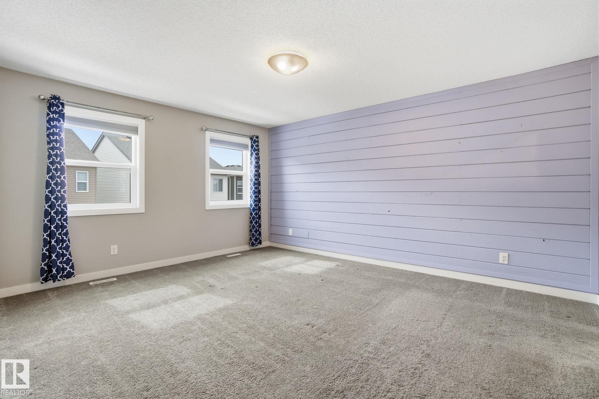 Spacious room featuring light grey carpet, two windows providing natural light, and a decorative accent wall with horizontal paneling - 1607 202 Street, Edmonton, AB - Photo Showing Other Room
