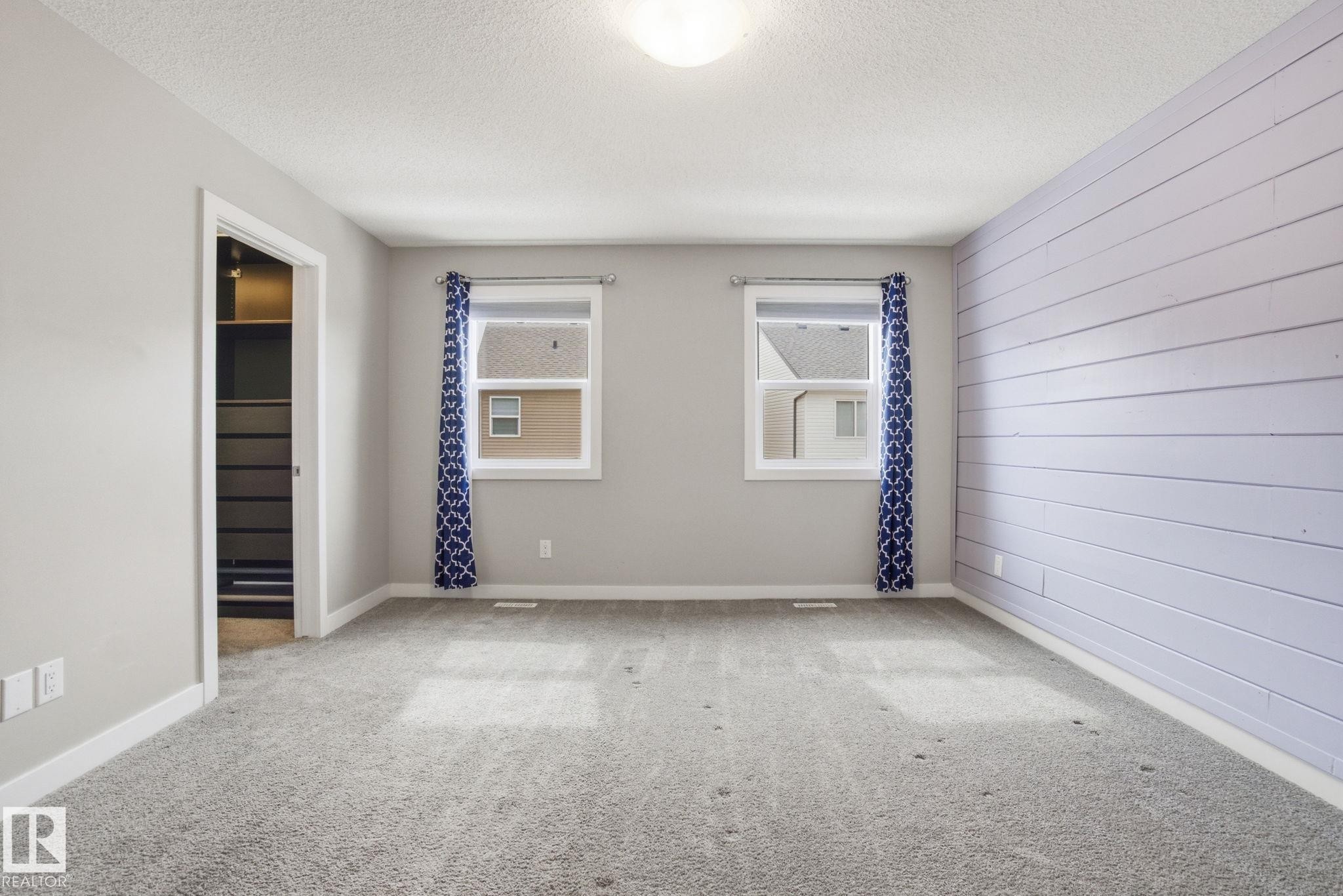 Spacious room featuring light grey walls, a textured accent wall, two windows, and grey carpeting - 1607 202 Street, Edmonton, AB - Indoor Photo Showing Other Room
