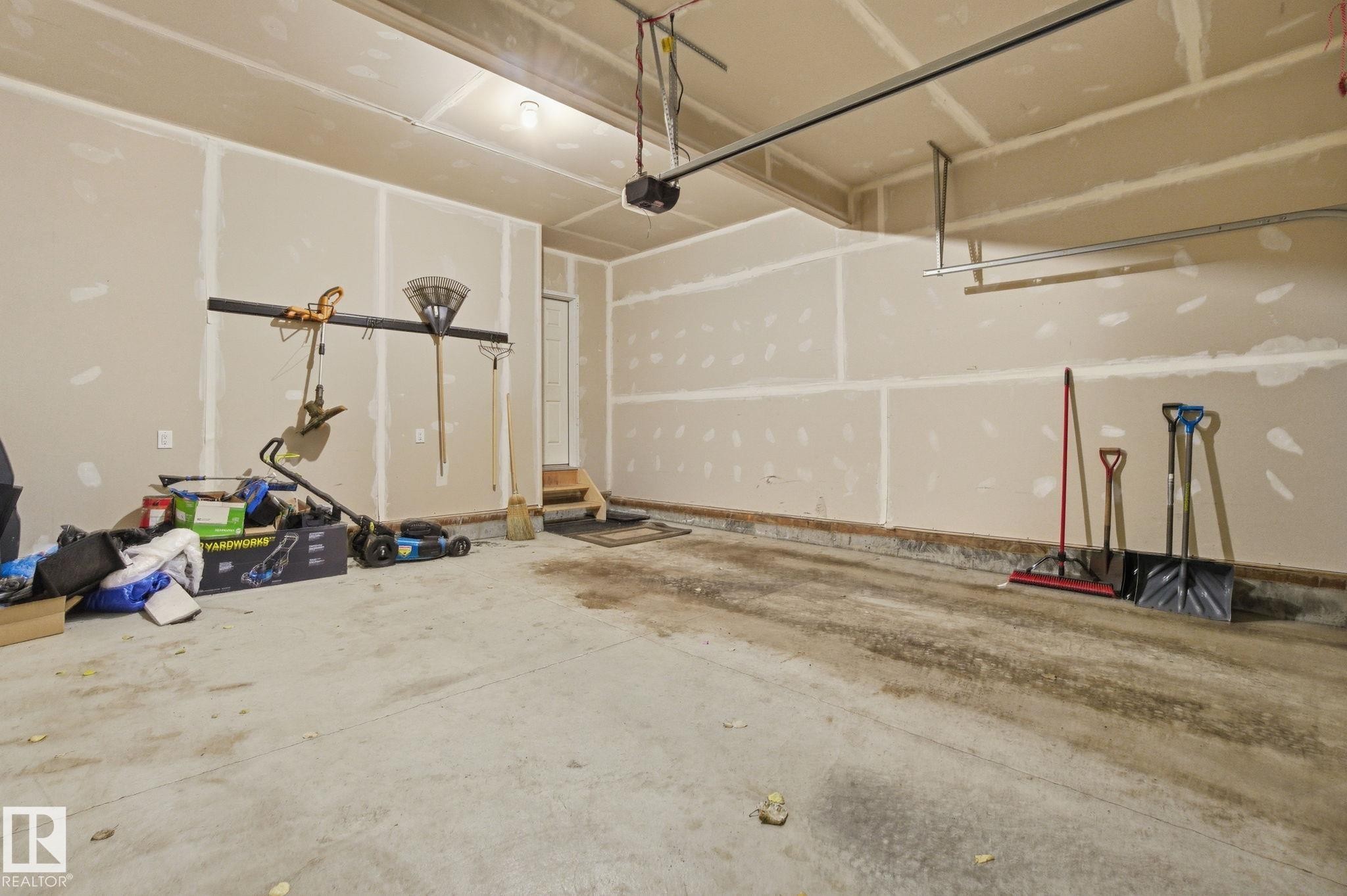 The property features an attached garage with unfinished walls, a concrete floor, and overhead garage door tracks - 1607 202 Street, Edmonton, AB - Indoor Photo Showing Garage
