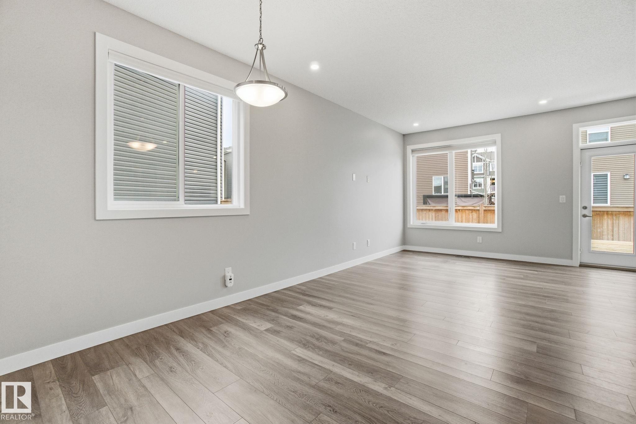 Bright interior space featuring light-colored walls, recessed ceiling lighting, and a modern light fixture - 1607 202 Street, Edmonton, AB - Indoor Photo Showing Living Room