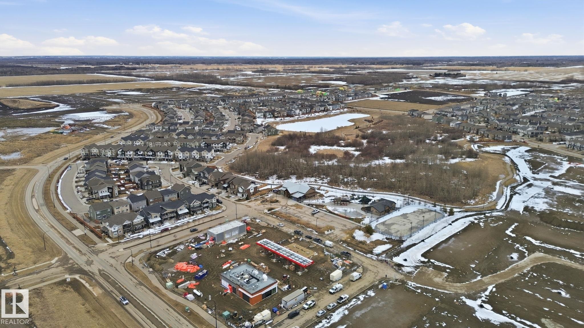 Aerial view showcasing a residential area with a curved road, surrounded by undeveloped land and a body of water - 1607 202 Street, Edmonton, AB - Outdoor With View
