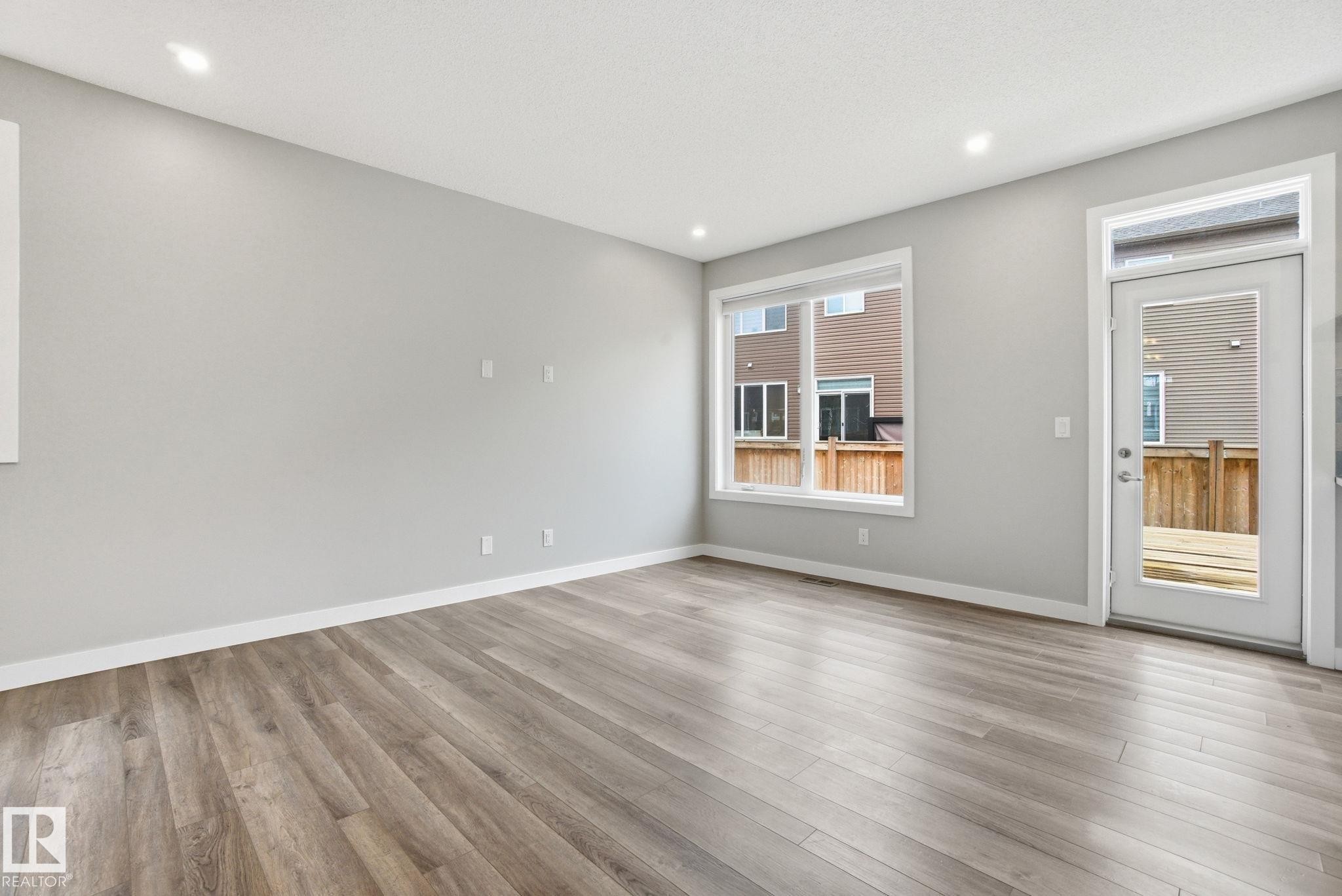 The property offers an open area with light-toned flooring, recessed lighting, a large window, and a glass-paneled door leading to an outdoor space - 1607 202 Street, Edmonton, AB - Indoor Photo Showing Other Room