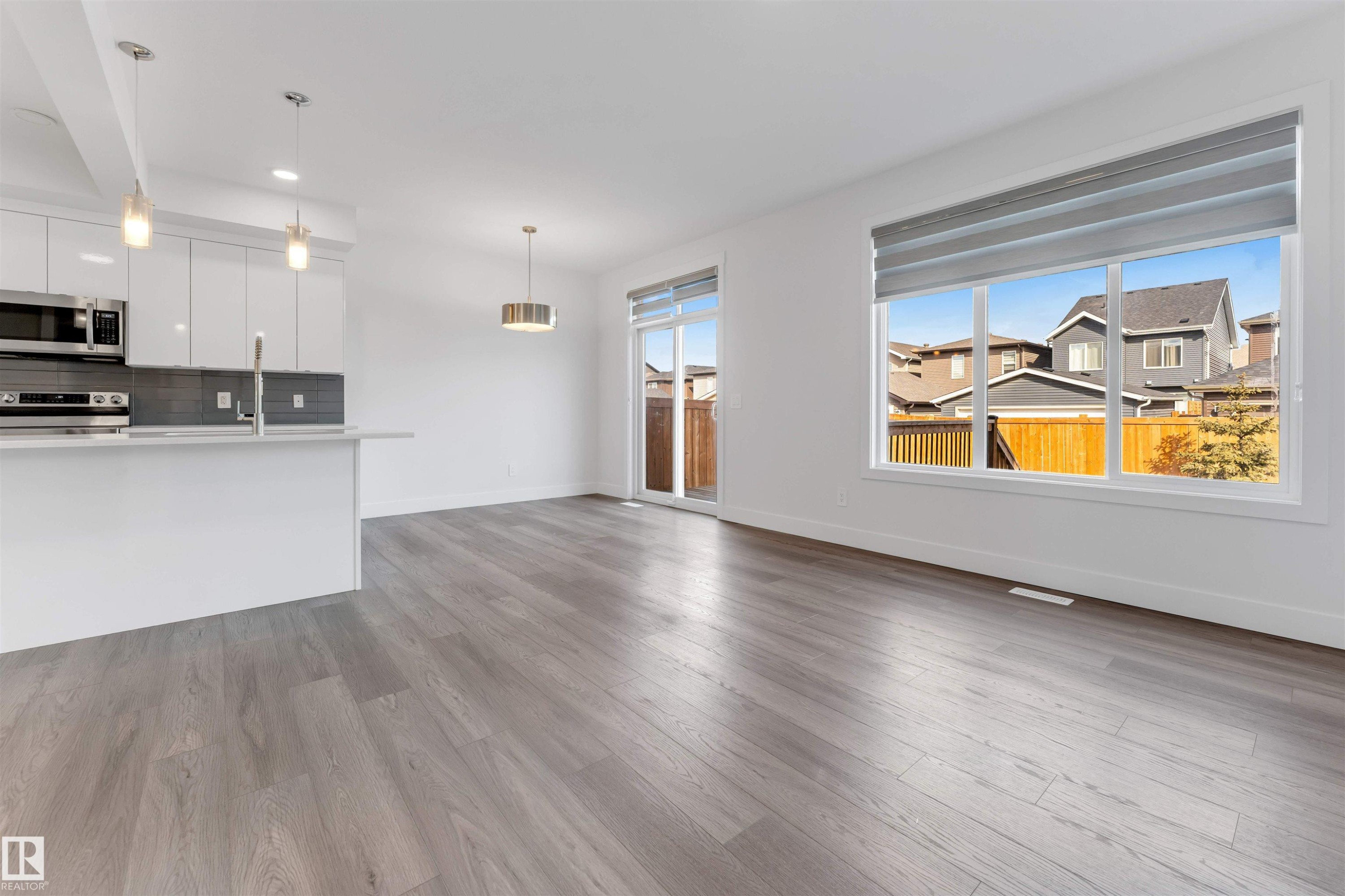 Open concept living space featuring wide plank flooring, a modern kitchen with white cabinetry and stainless steel appliances, and large windows providing natural light - 1663 Cavanagh Boulevard Sw, Edmonton, AB - Indoor Photo Showing Kitchen