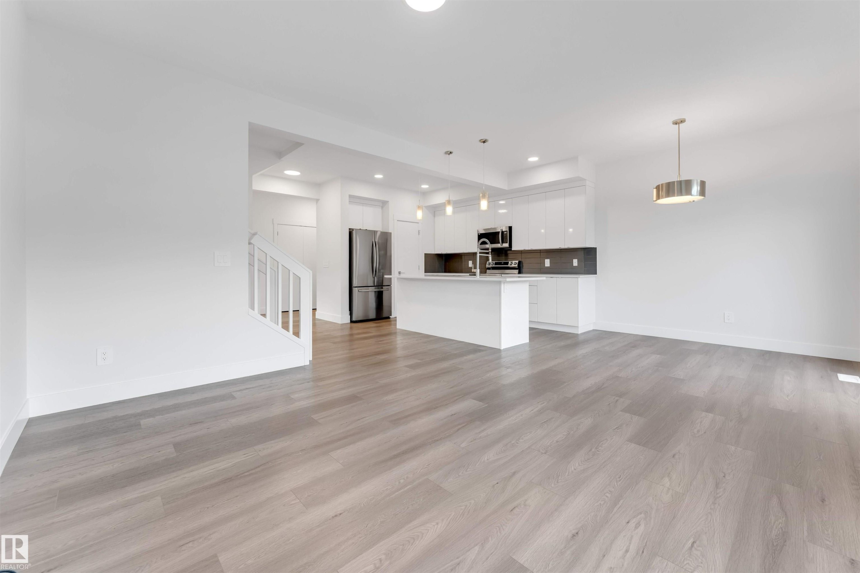 Open concept living area with light-toned flooring, featuring a modern kitchen with a central island and stainless steel appliances - 1663 Cavanagh Boulevard Sw, Edmonton, AB - Indoor Photo Showing Kitchen