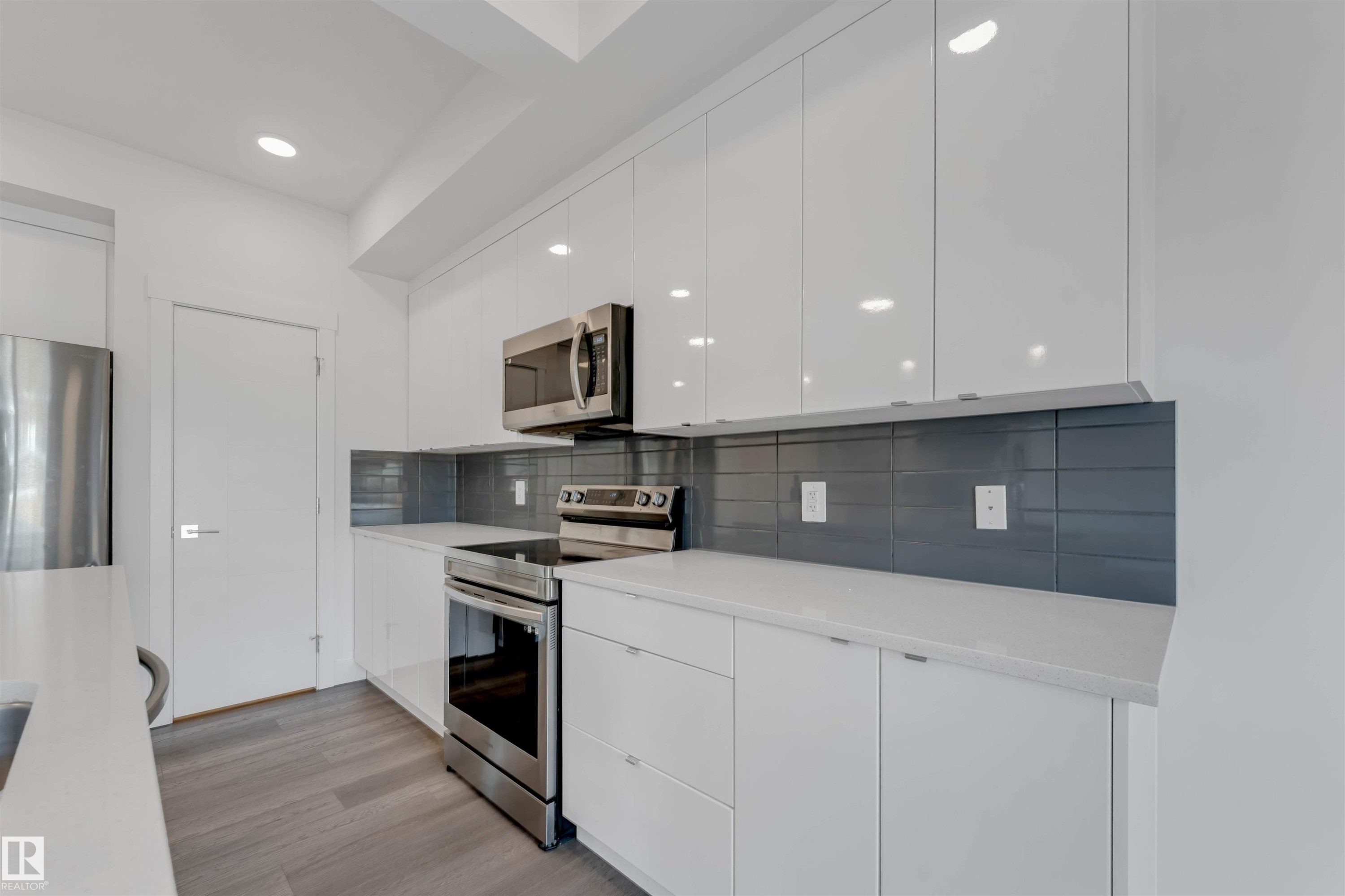 The kitchen features white cabinetry, stainless steel appliances, a dark grey tiled backsplash, and light countertops - 1663 Cavanagh Boulevard Sw, Edmonton, AB - Indoor Photo Showing Kitchen