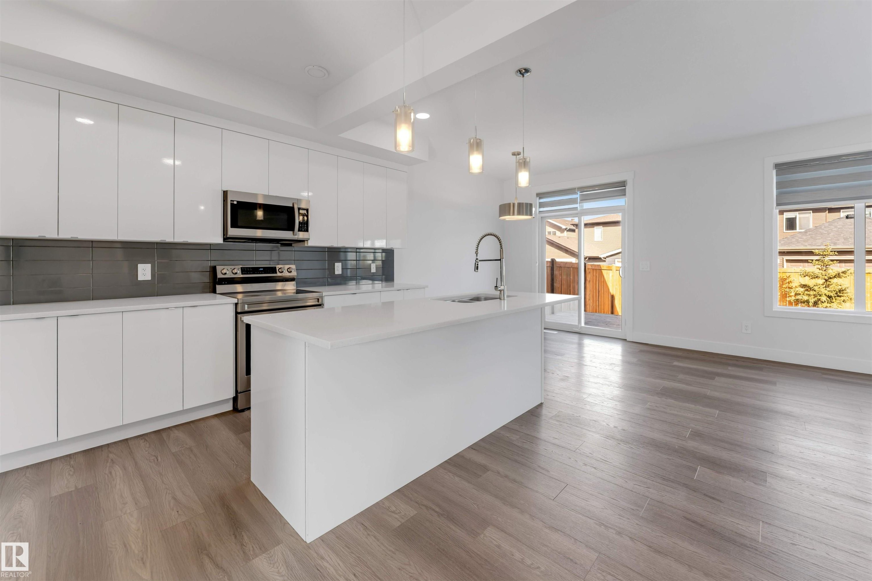 Modern kitchen featuring white cabinetry, stainless steel appliances, a center island with a sink, and pendant lighting - 1663 Cavanagh Boulevard Sw, Edmonton, AB - Indoor Photo Showing Kitchen