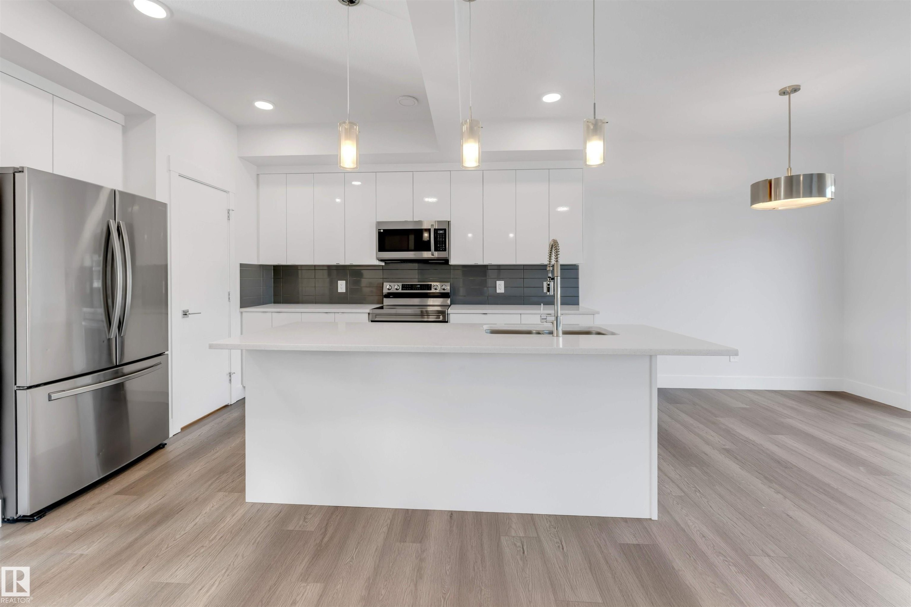 Modern kitchen featuring a white island with a sink, white cabinetry, stainless steel appliances, and a gray tiled backsplash - 1663 Cavanagh Boulevard Sw, Edmonton, AB - Indoor Photo Showing Kitchen With Upgraded Kitchen