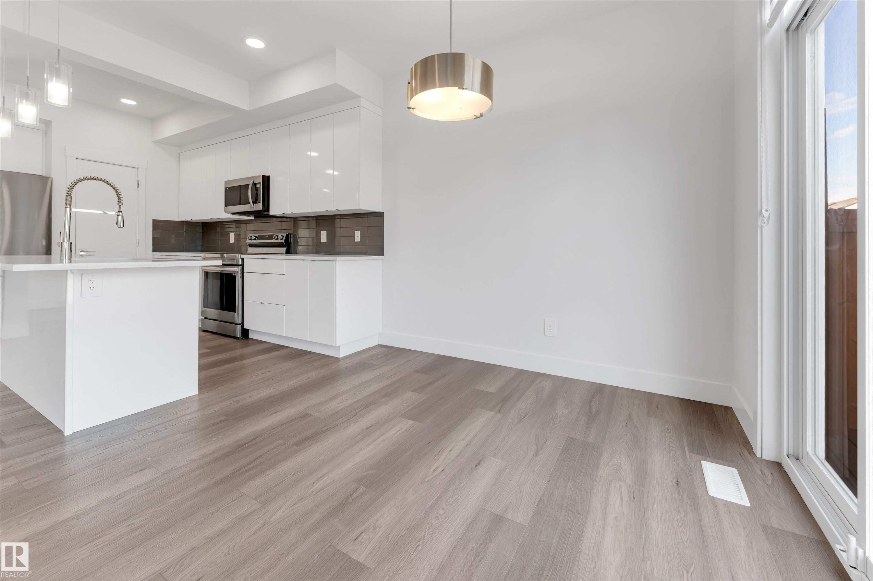 The property features a kitchen with white cabinetry, stainless steel appliances, and a kitchen island with a sink - 1663 Cavanagh Boulevard Sw, Edmonton, AB - Indoor Photo Showing Kitchen