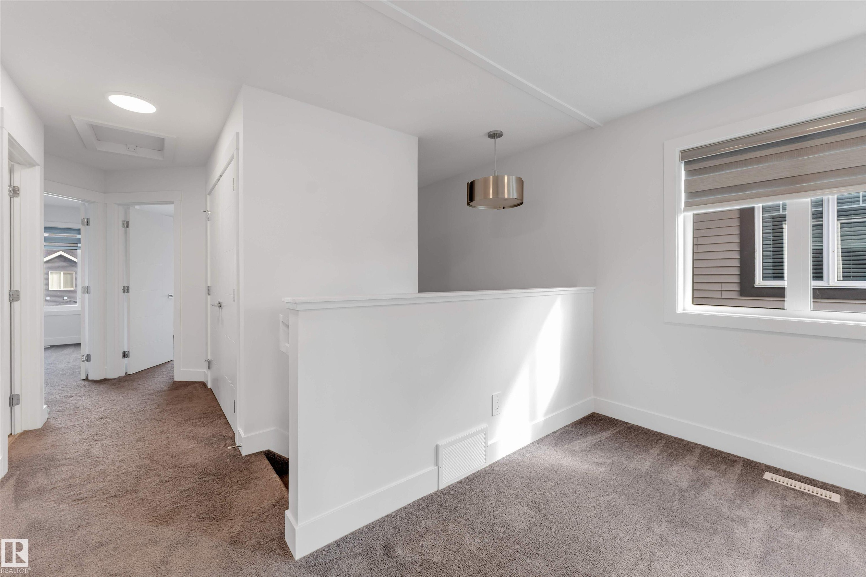 This area features light-colored walls, carpeted flooring, and a large window providing natural light - 1663 Cavanagh Boulevard Sw, Edmonton, AB - Indoor Photo Showing Other Room