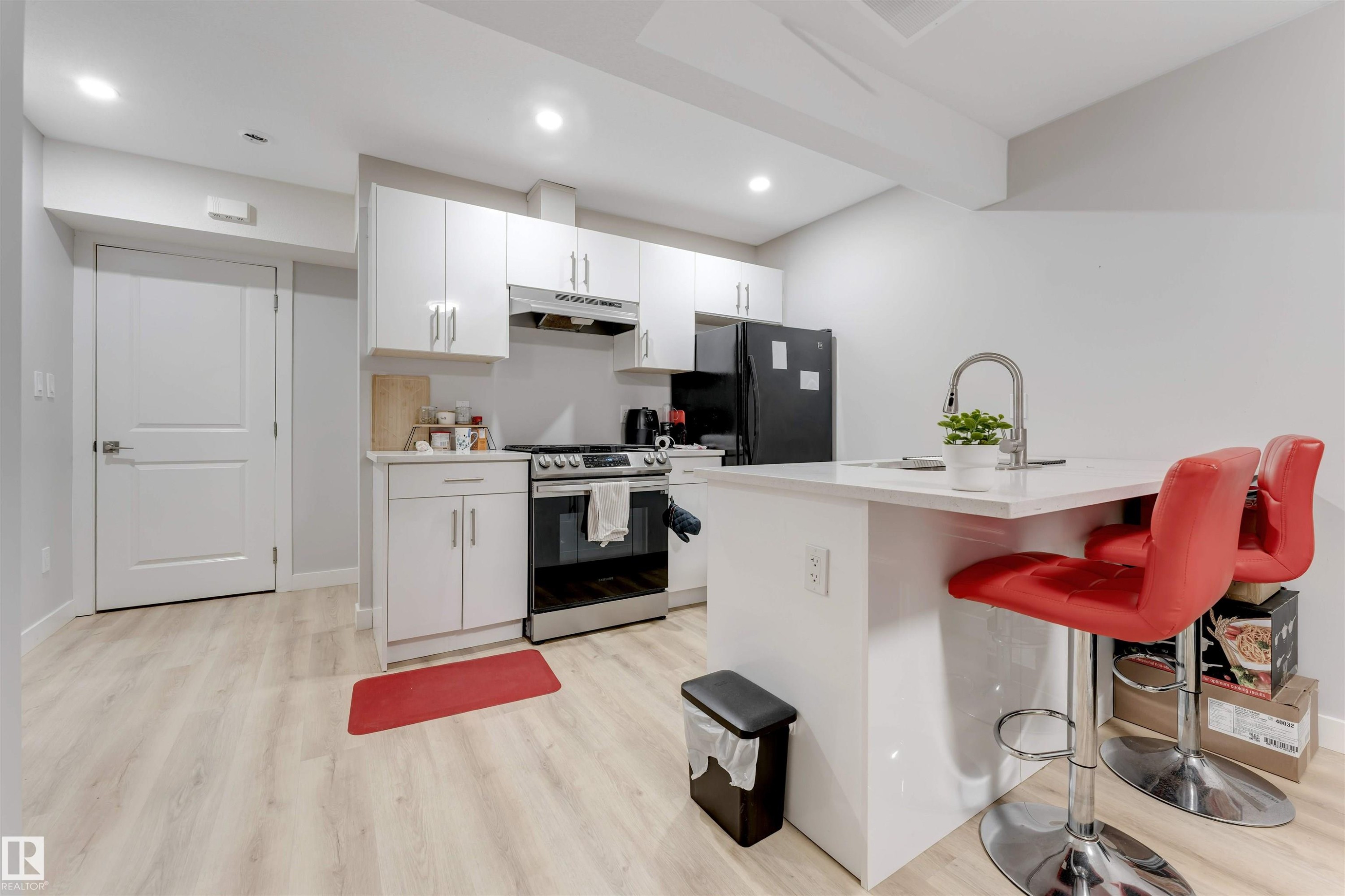 The kitchen features light wood-style flooring, white cabinetry, a stainless steel oven and range, and a kitchen island with a sink and seating - 1663 Cavanagh Boulevard Sw, Edmonton, AB - Indoor Photo Showing Kitchen With Upgraded Kitchen