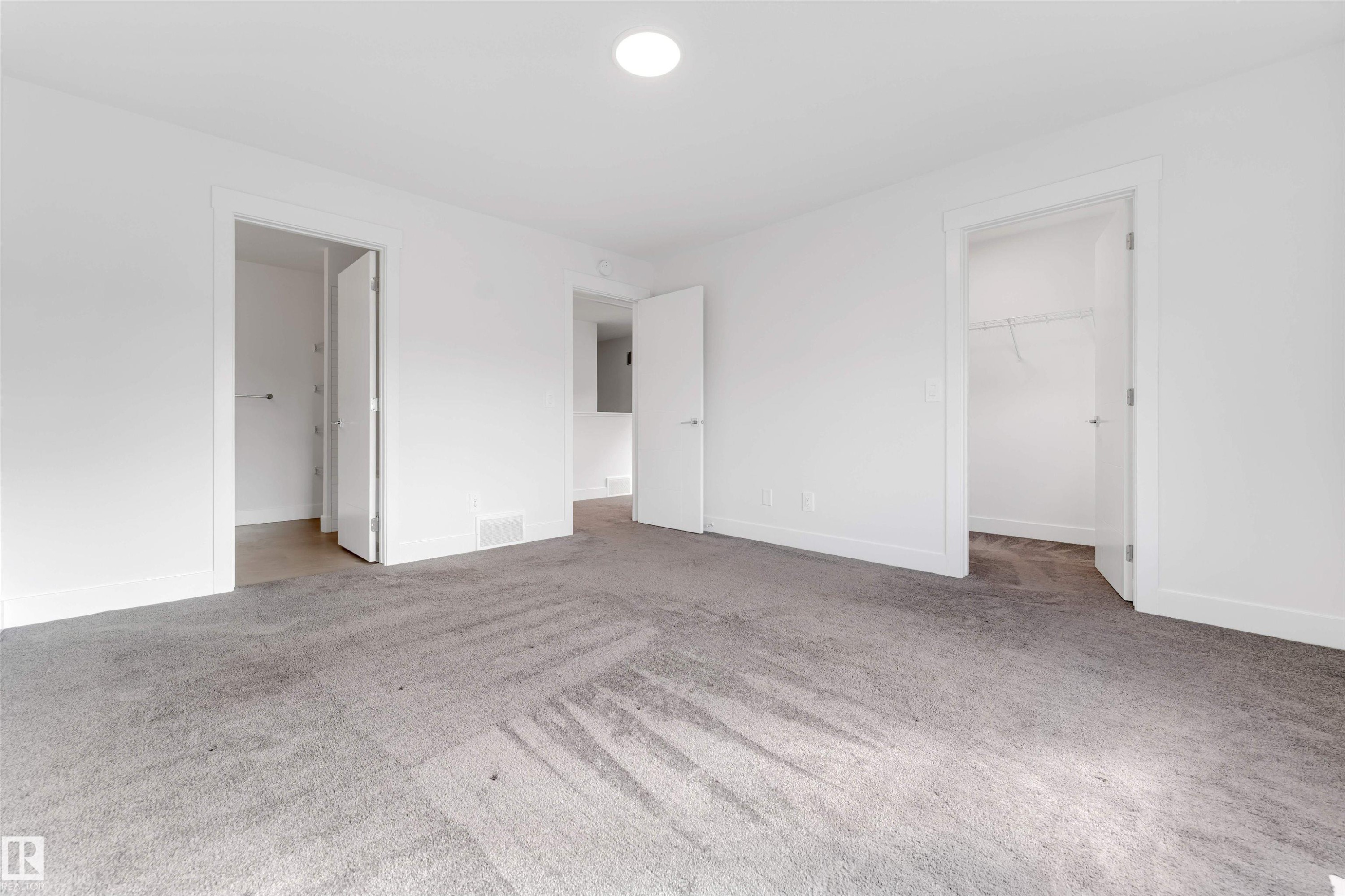 The property features a spacious room with light grey carpeting, white walls, and white trim - 1663 Cavanagh Boulevard Sw, Edmonton, AB - Indoor Photo Showing Other Room