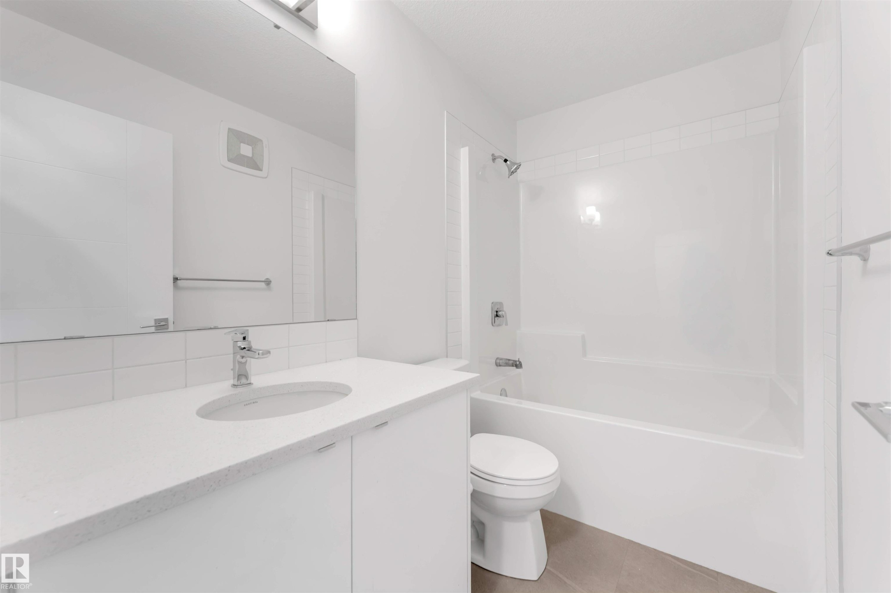 The bathroom features a vanity with a white countertop and an integrated sink, a large mirror, and a bathtub with a shower - 1663 Cavanagh Boulevard Sw, Edmonton, AB - Indoor Photo Showing Bathroom