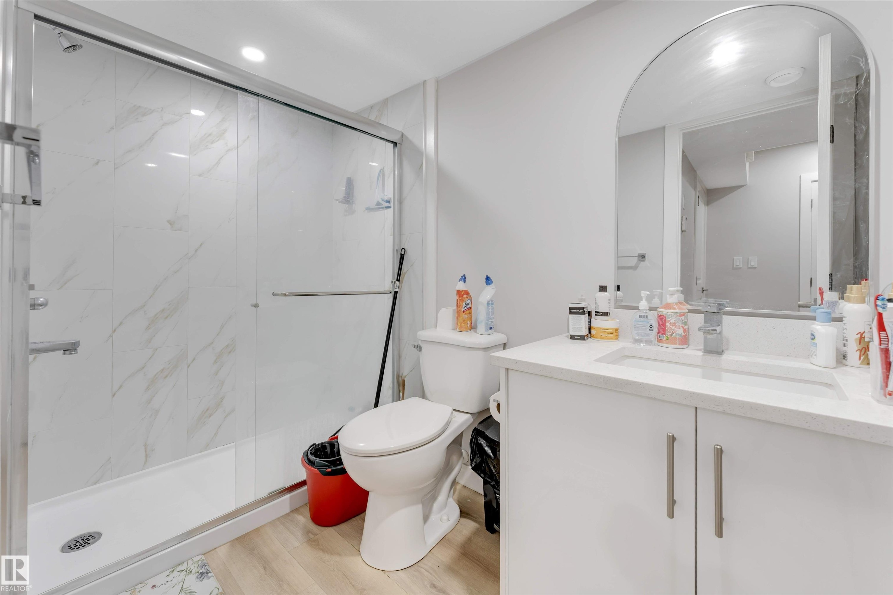 Bathroom featuring a spacious shower with sliding glass doors, white tiled walls with subtle veining, and a contemporary vanity with a white countertop and an arched mirror - 1663 Cavanagh Boulevard Sw, Edmonton, AB - Indoor Photo Showing Bathroom