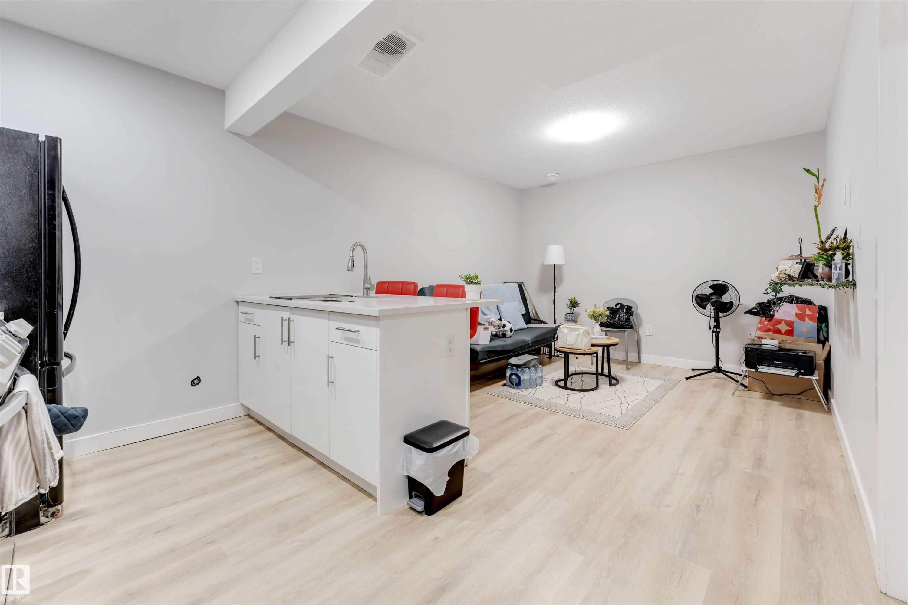 This open-concept living area features light-toned flooring, a bright recessed ceiling light, and a kitchen island with a sink and white cabinetry - 1663 Cavanagh Boulevard Sw, Edmonton, AB - Indoor Photo Showing Other Room