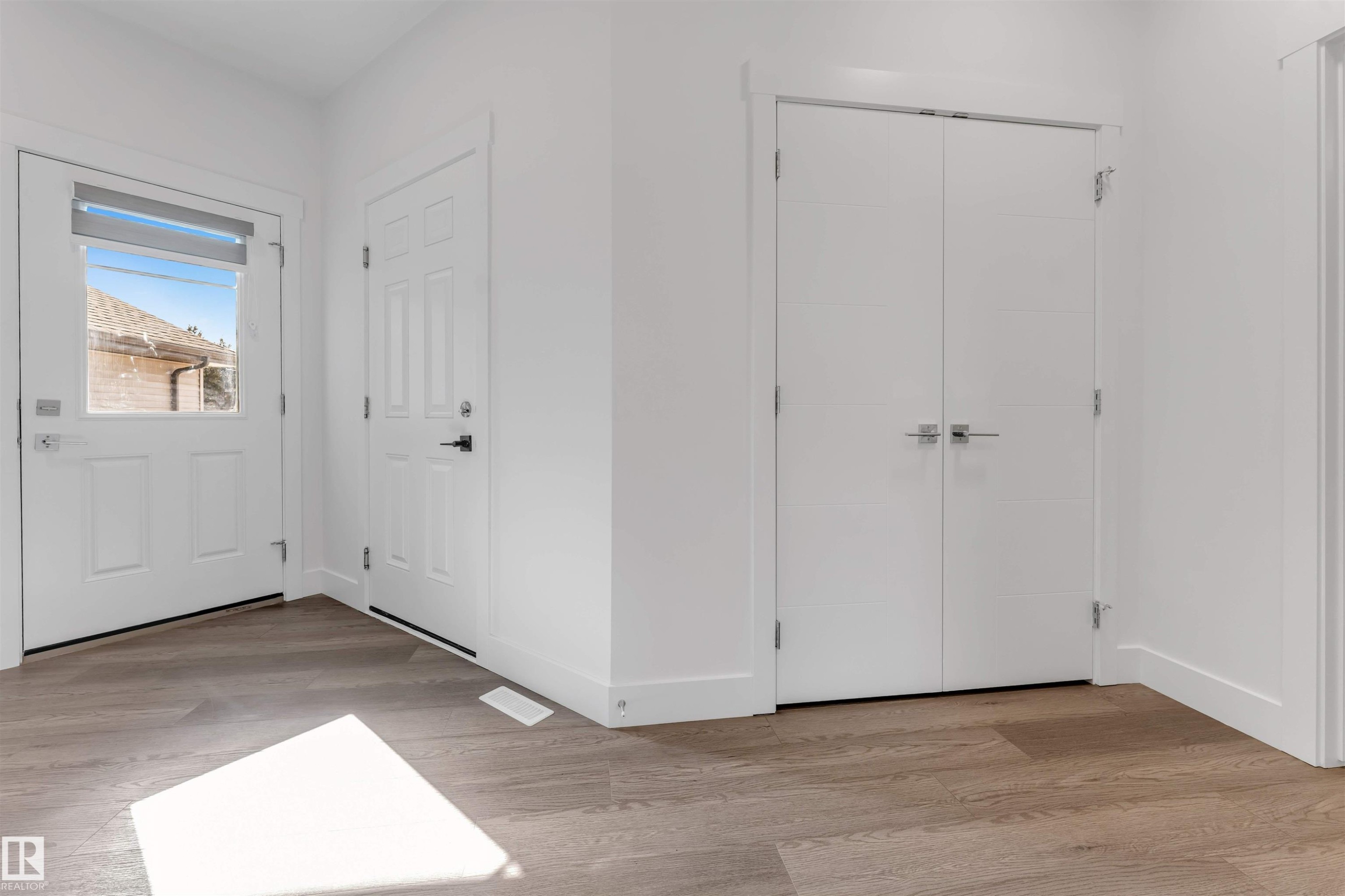 Entryway featuring light wood-look flooring, white walls, and white doors with dark hardware - 1663 Cavanagh Boulevard Sw, Edmonton, AB - Indoor Photo Showing Other Room