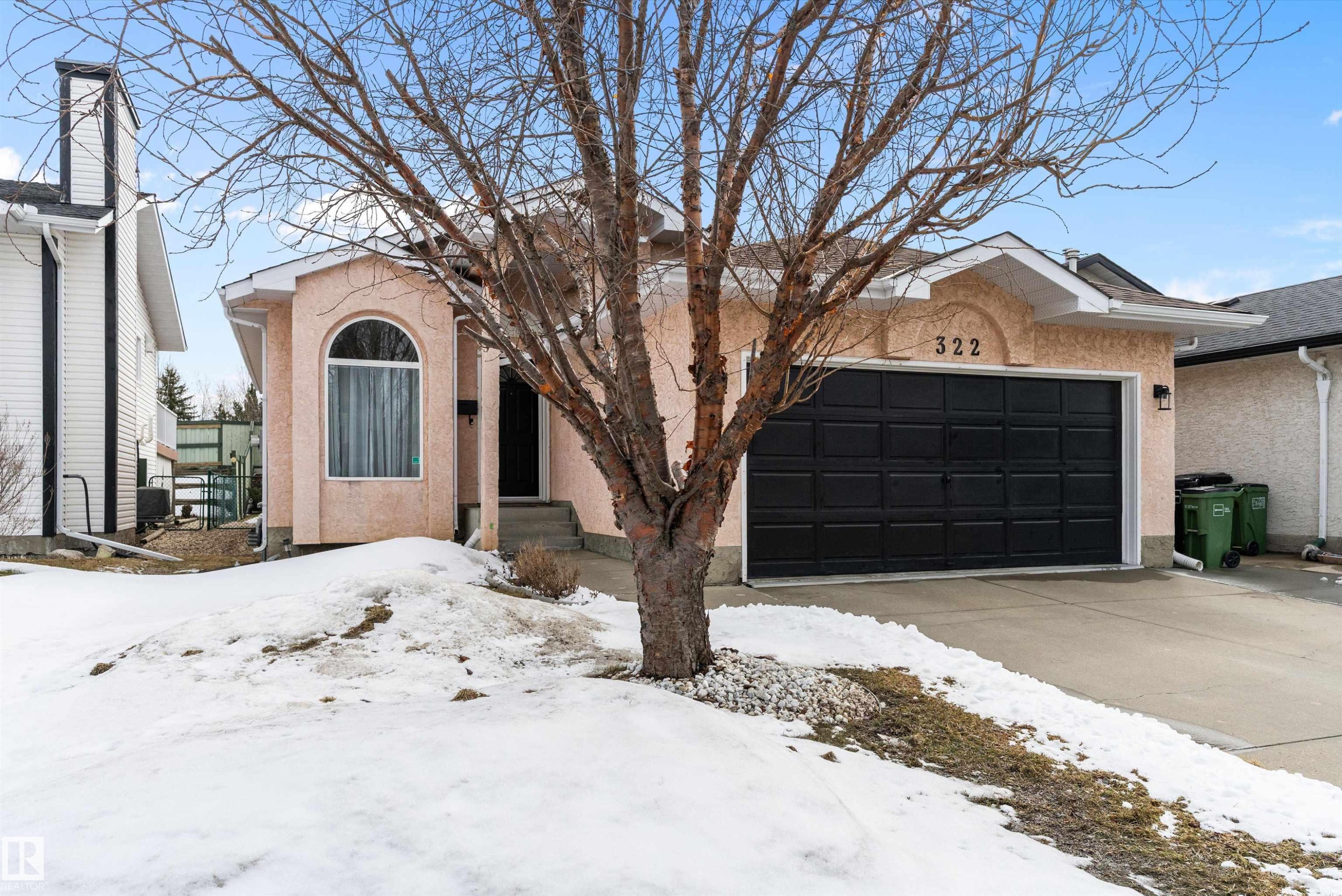 The property features a stucco exterior, an arched window, and an attached garage with a black door - 322 Pearson Crescent, Edmonton, AB - Outdoor With Facade