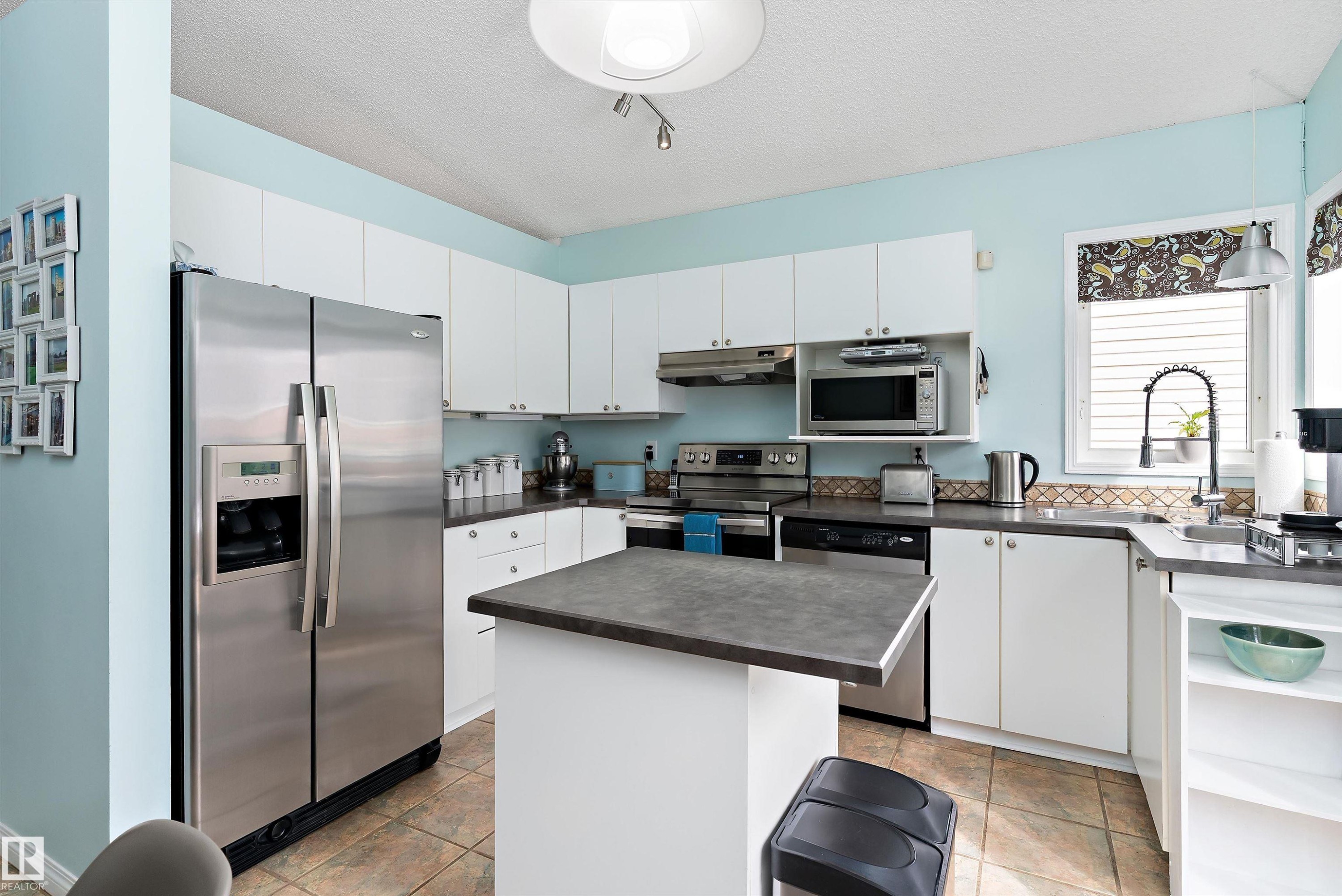 The kitchen features white cabinetry, stainless steel appliances, a center island with a dark countertop, and tiled flooring - 322 Pearson Crescent, Edmonton, AB - Indoor Photo Showing Kitchen With Double Sink