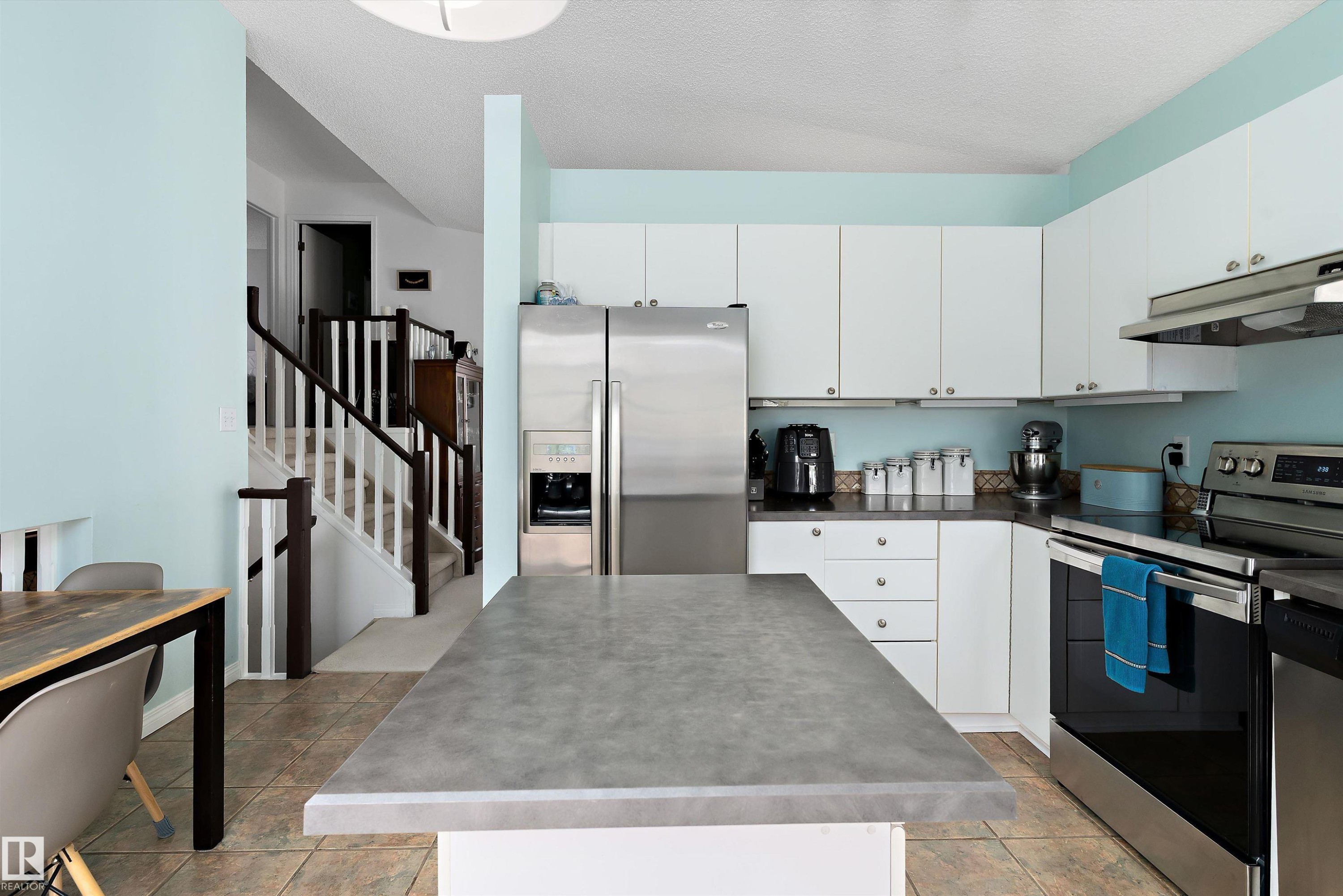 The kitchen features white cabinetry, stainless steel appliances, and a central island with a grey countertop - 322 Pearson Crescent, Edmonton, AB - Indoor Photo Showing Kitchen