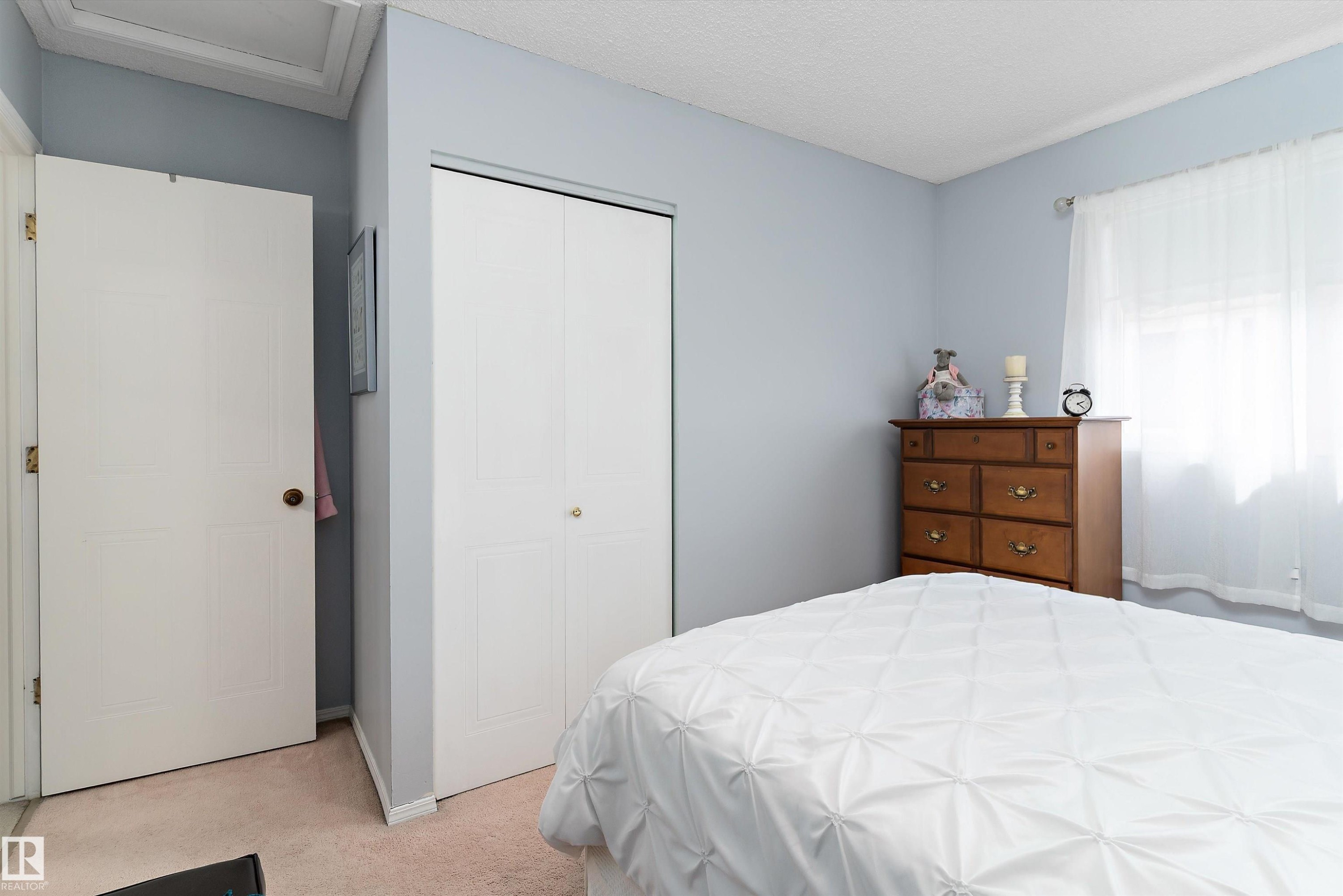 The room features light blue walls, a white bi-fold closet door, and a window with sheer white curtains - 322 Pearson Crescent, Edmonton, AB - Indoor Photo Showing Bedroom