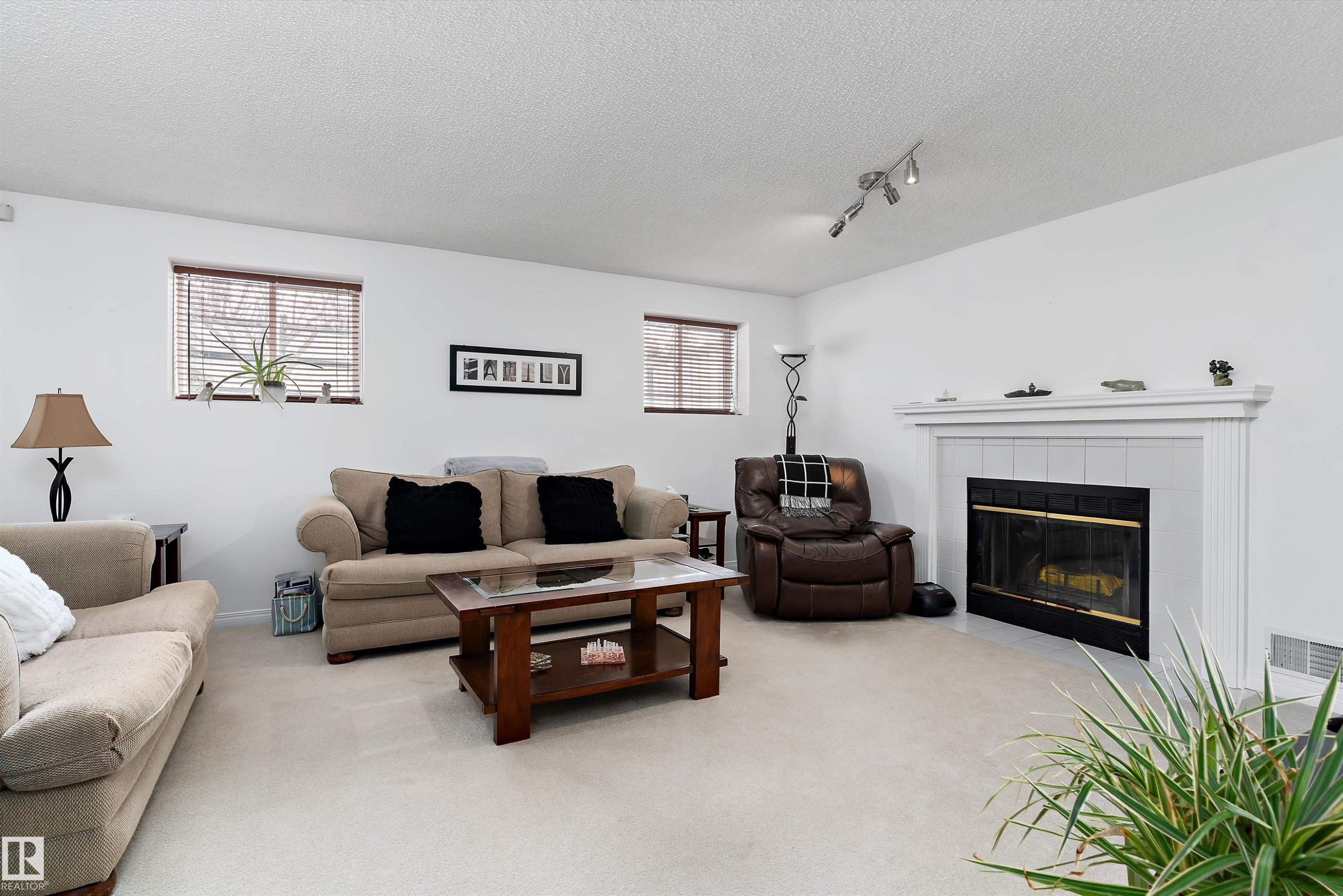 The living area features light-colored carpeting, white walls, and a fireplace with a white mantel and black surround - 322 Pearson Crescent, Edmonton, AB - Indoor Photo Showing Living Room With Fireplace