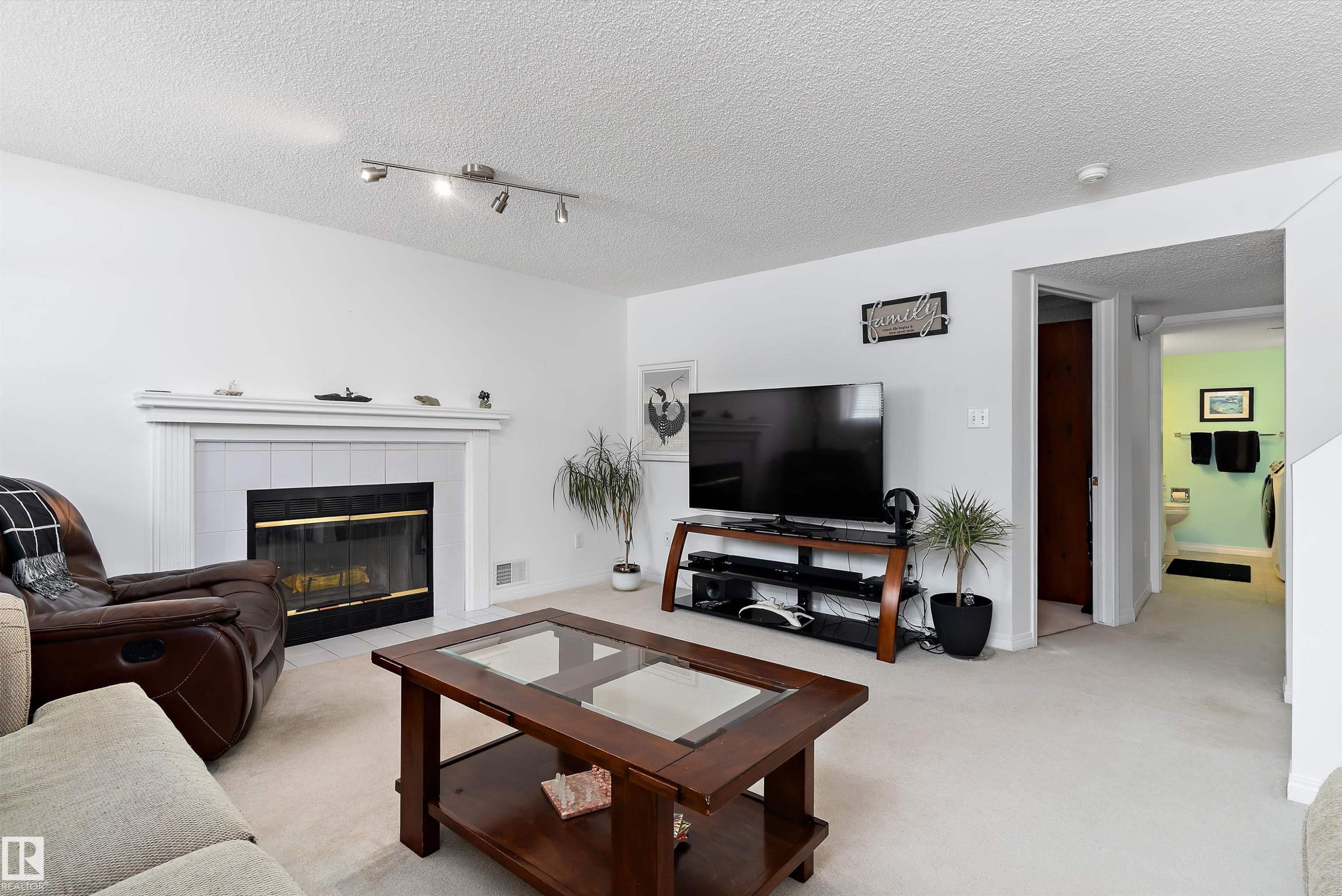 The living area features a fireplace with a white mantel and tiled surround, light-colored carpeting, and track lighting - 322 Pearson Crescent, Edmonton, AB - Indoor Photo Showing Living Room With Fireplace