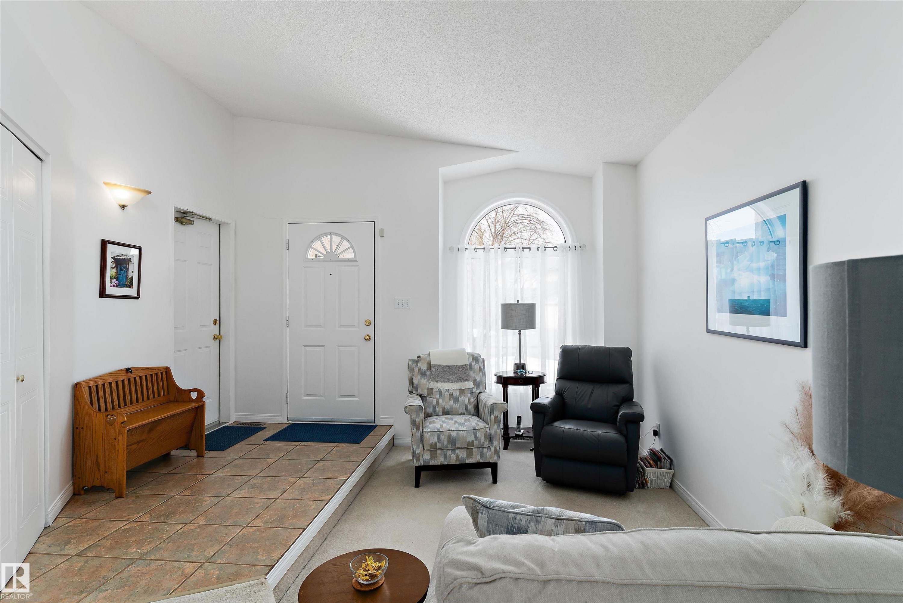 The bright living area features a front entry door with an arched window, an additional arched window with sheer curtains, and a tiled entryway - 322 Pearson Crescent, Edmonton, AB - Indoor