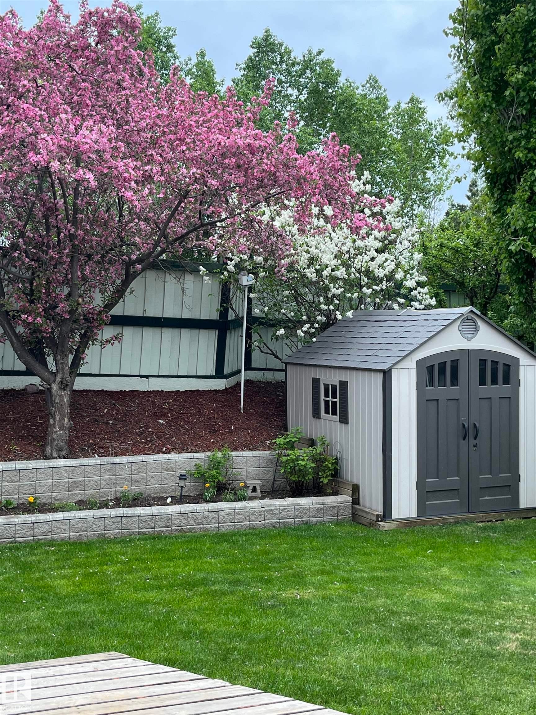 The property features a well-maintained lawn, an outdoor storage shed with double doors and a window, and a raised garden bed with stone retaining walls - 322 Pearson Crescent, Edmonton, AB - Outdoor