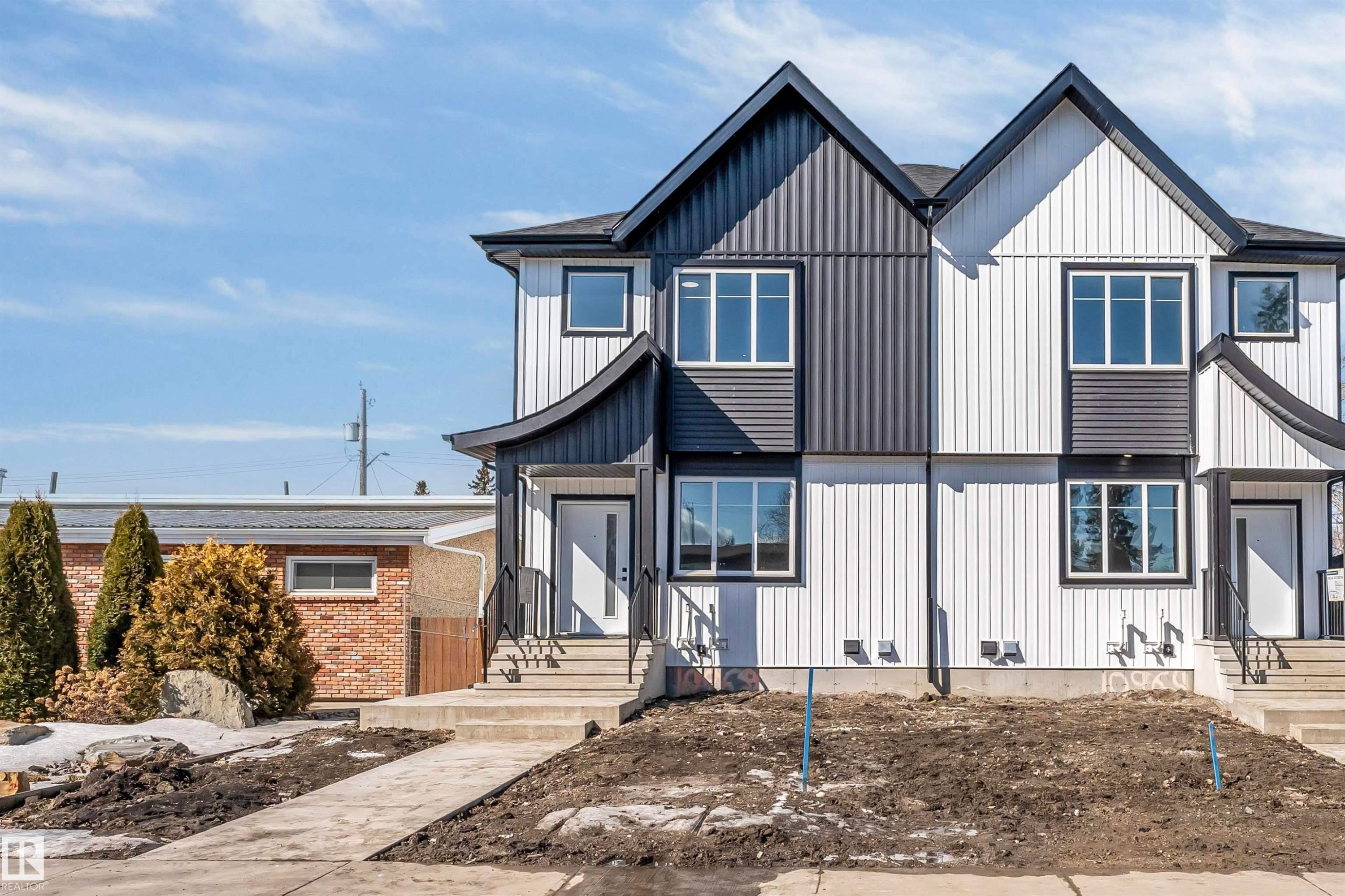 Modern duplex featuring a striking black and white exterior, large windows, and a concrete pathway leading to the entrance - 10962 157 Street, Edmonton, AB - Outdoor