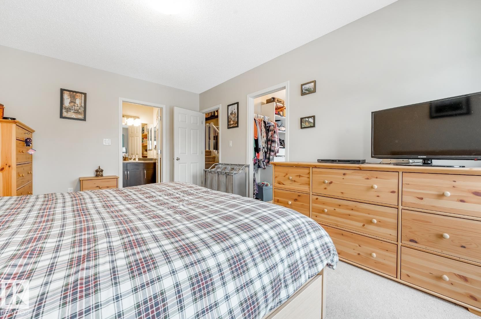 This room features light-colored walls and carpeting, with a partial view into a bathroom with a vanity and mirror, and an open closet - 3109 Carpenter Landing, Edmonton, AB - Indoor Photo Showing Bedroom