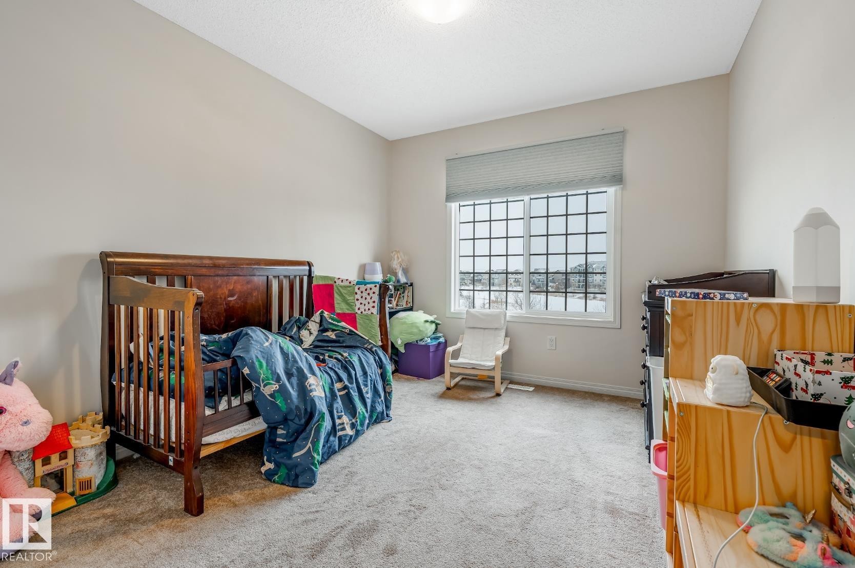 This room features neutral-toned walls, a textured carpet, and a window with a grid pattern and blinds, allowing for natural light - 3109 Carpenter Landing, Edmonton, AB - Indoor Photo Showing Bedroom