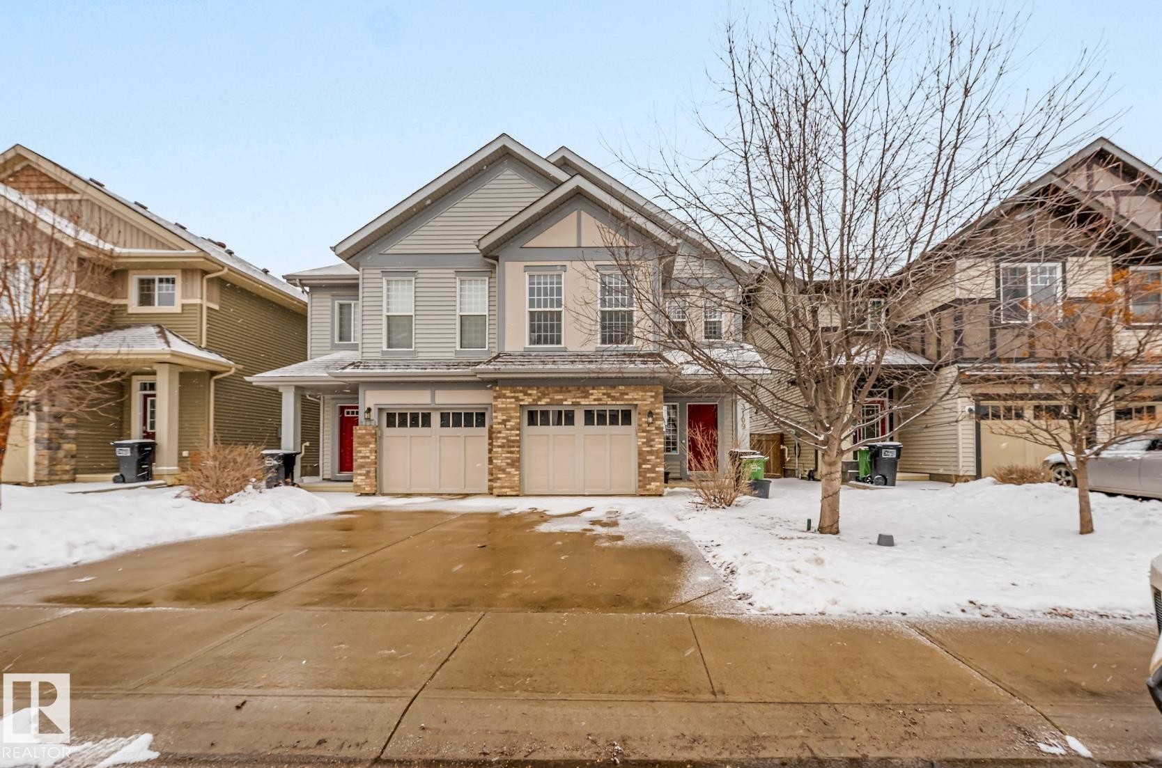 This property features a two-story exterior with light-colored siding, stone accents, and a two-car garage - 3109 Carpenter Landing, Edmonton, AB - Outdoor With Facade