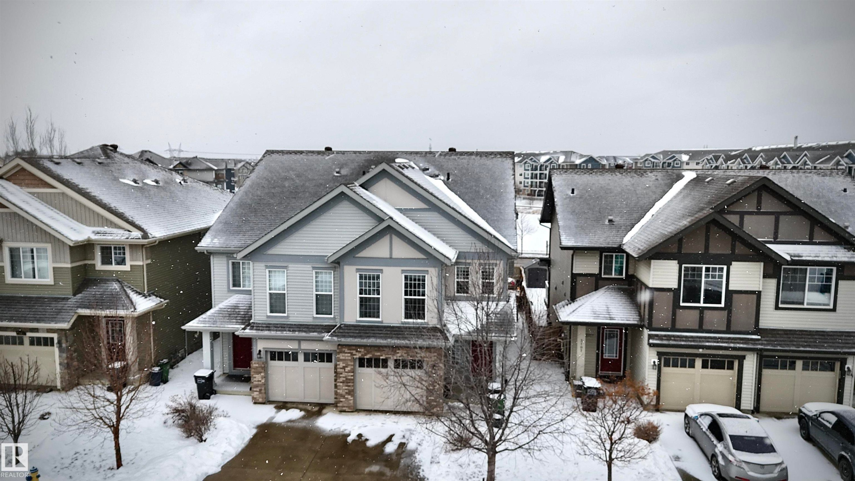 The property features a two-story exterior with light blue siding and stone accents on the lower level, a two-car garage, and a red front door - 3109 Carpenter Landing, Edmonton, AB - Outdoor With Facade